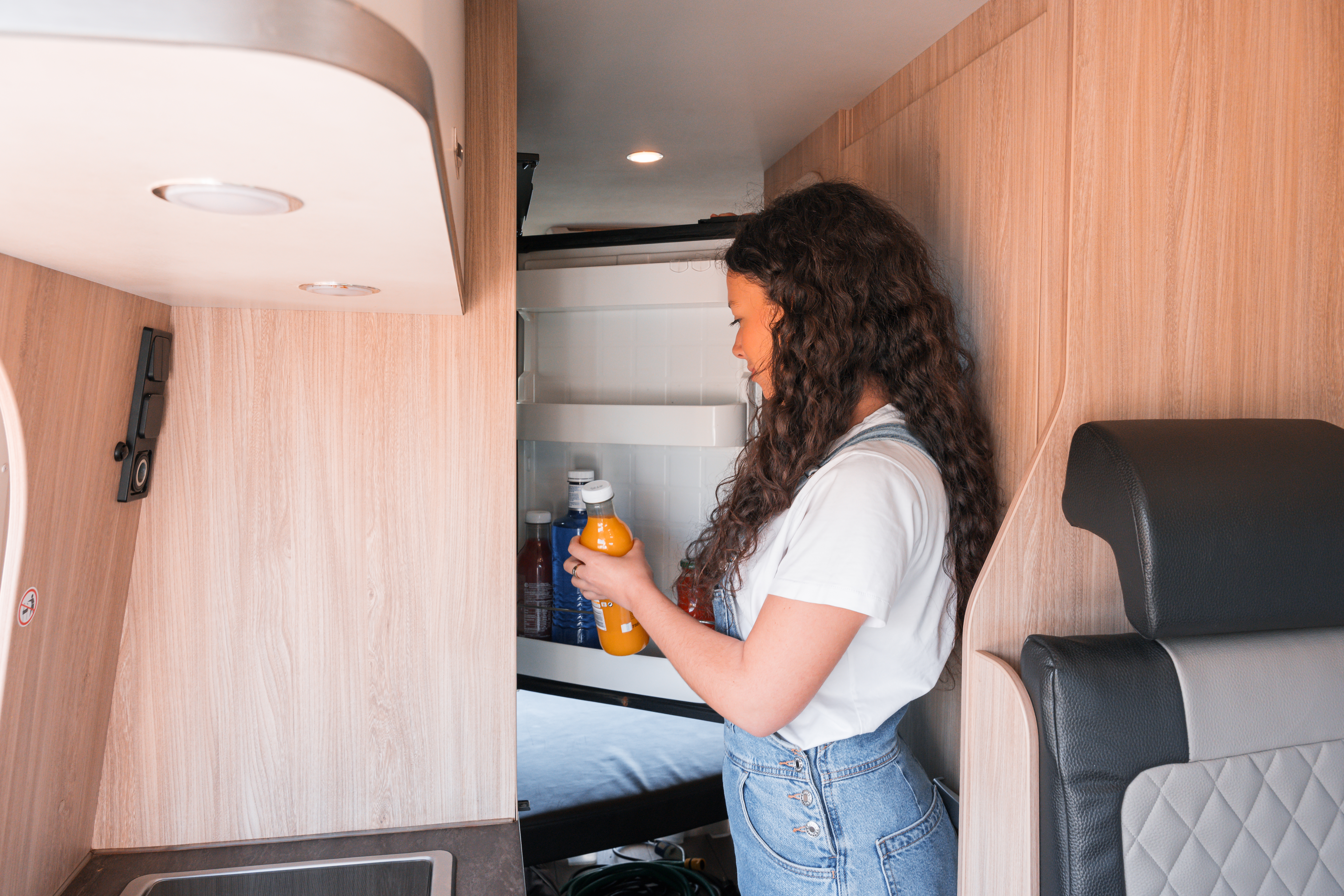 Person taking a juice bottle from a refrigerator inside a modern camper van with wooden interior.