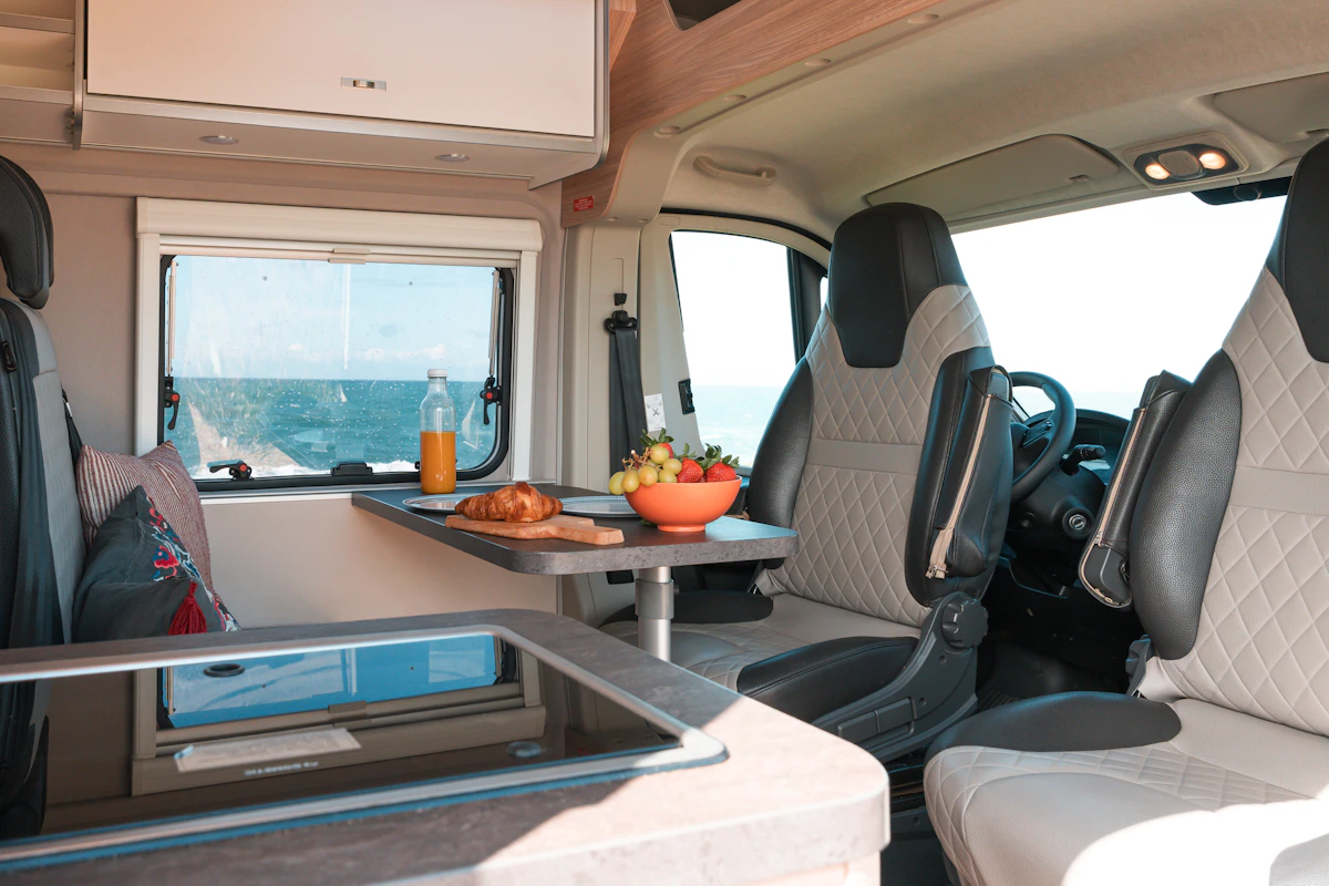 Interior of a campervan with a dining table, food, drinks, and a scenic view through the window.