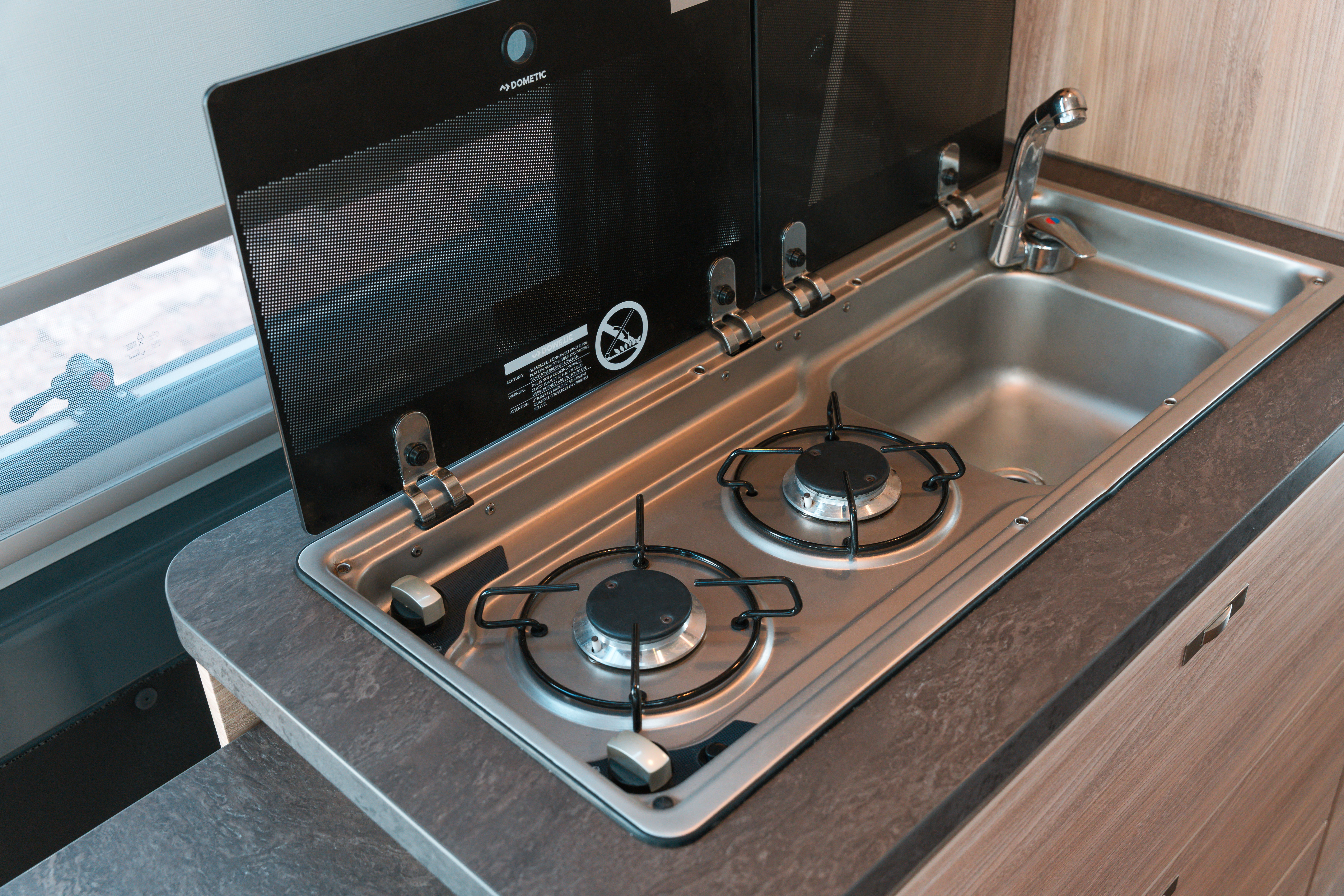 Modern campervan kitchenette with two-burner gas stove and stainless steel sink, set in a compact countertop.