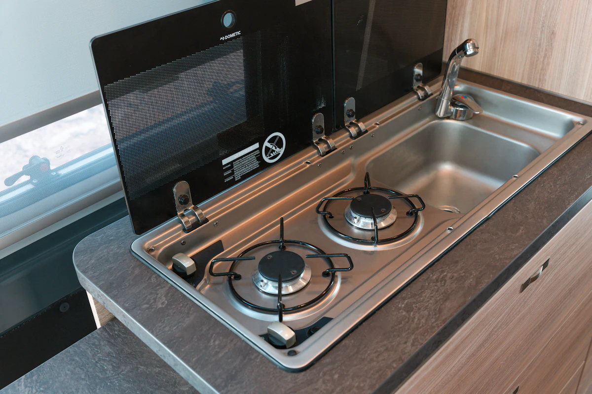 Modern campervan kitchenette with two-burner gas stove and stainless steel sink, set in a compact countertop.
