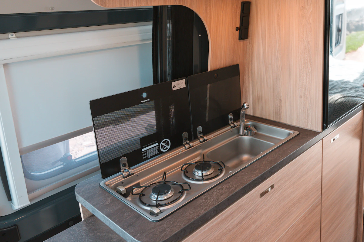 Modern campervan kitchen with two-burner gas stove, stainless steel sink, and faucet on a compact countertop.