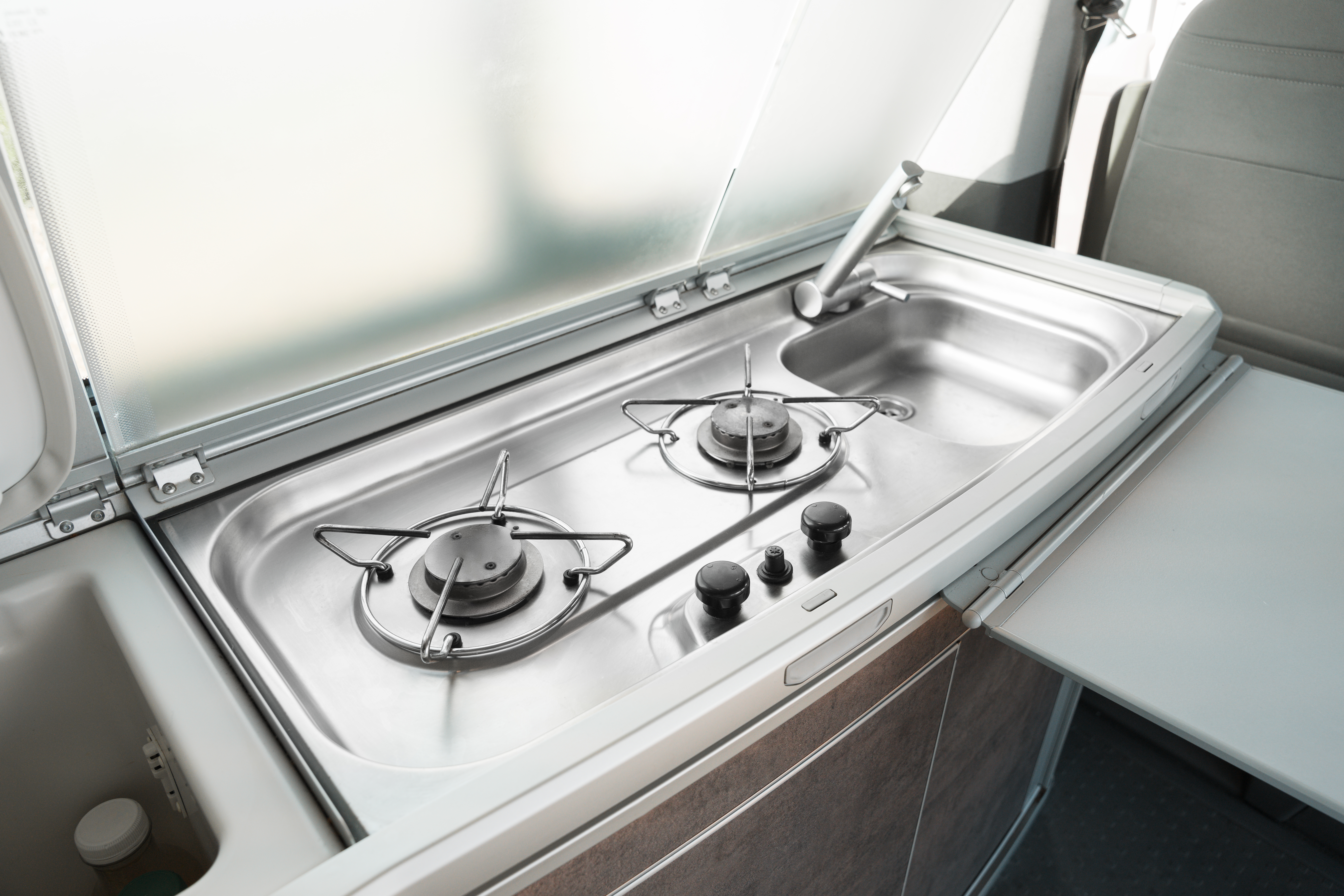 Modern campervan kitchen with two-burner gas stove, stainless steel sink, and closed storage compartments.