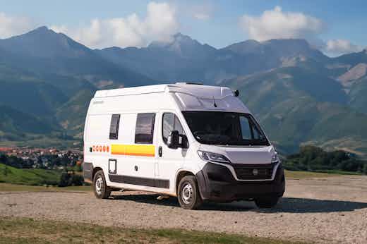 Active Bunk EU Hero White campervan parked on gravel with scenic mountain landscape and blue sky in the background.