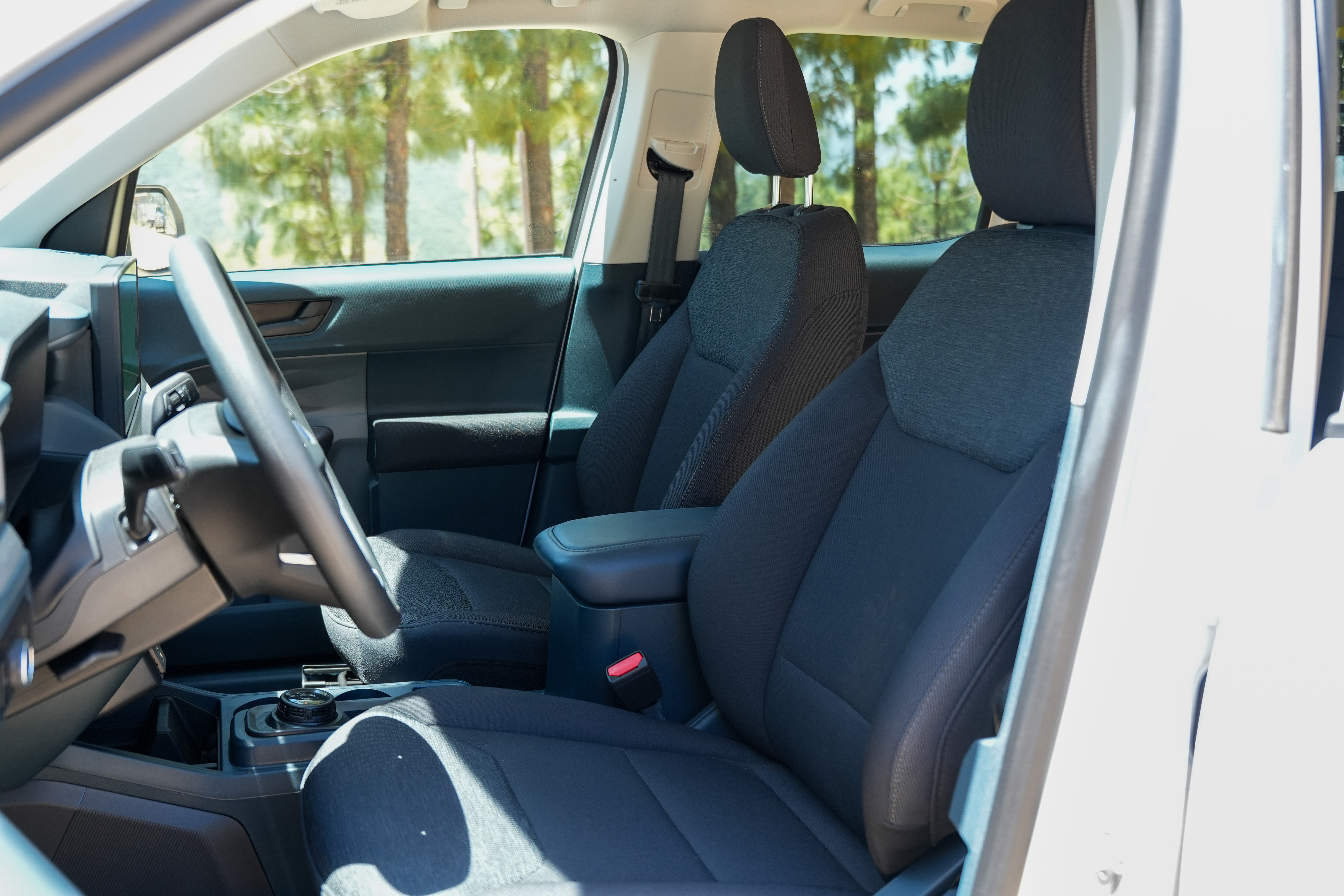 Front seats and dashboard of a modern campervan with black upholstery, photographed from the open passenger-side door.