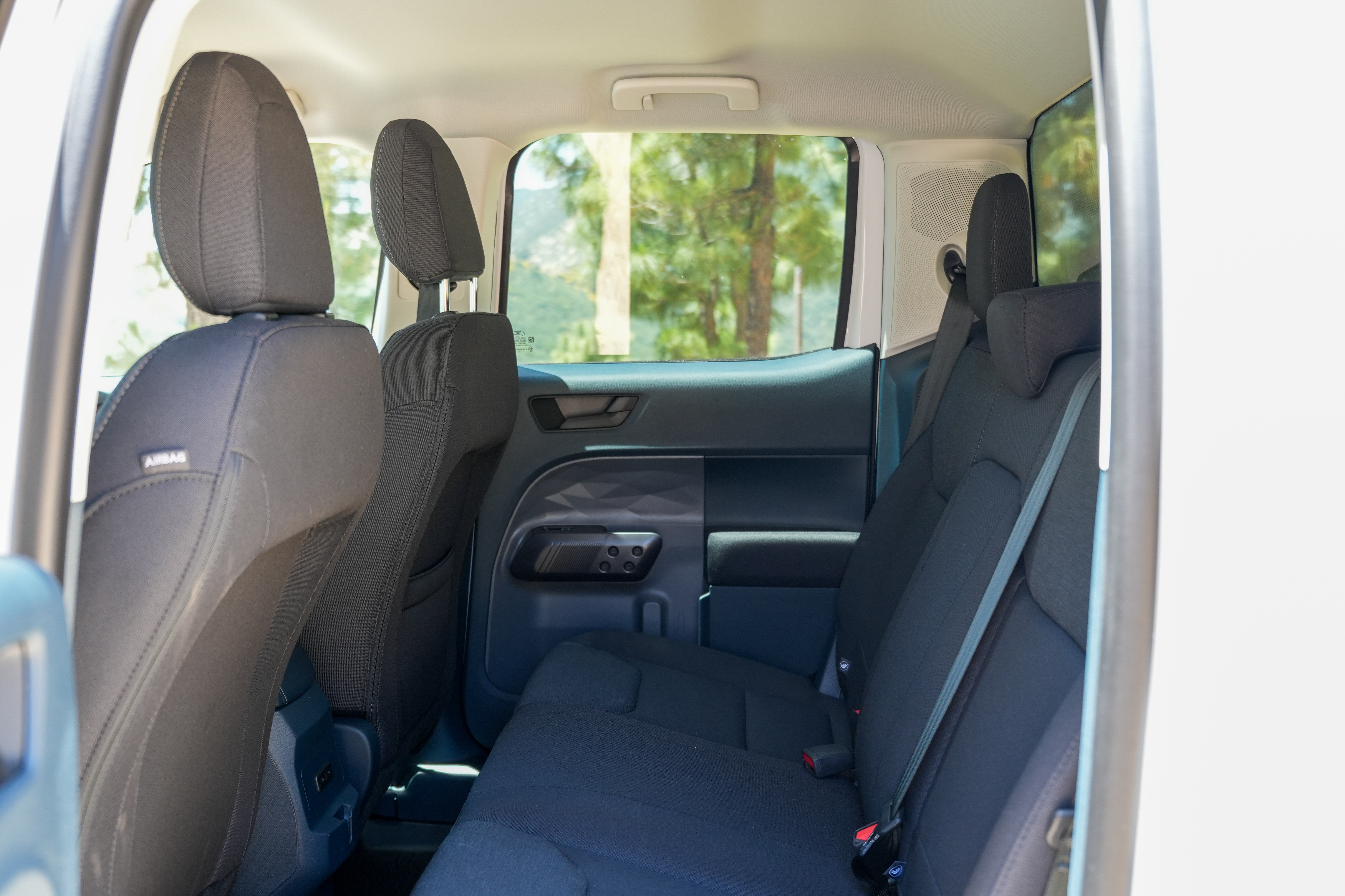 Interior view of a camper van’s back seats with black upholstery and natural light coming through the windows.