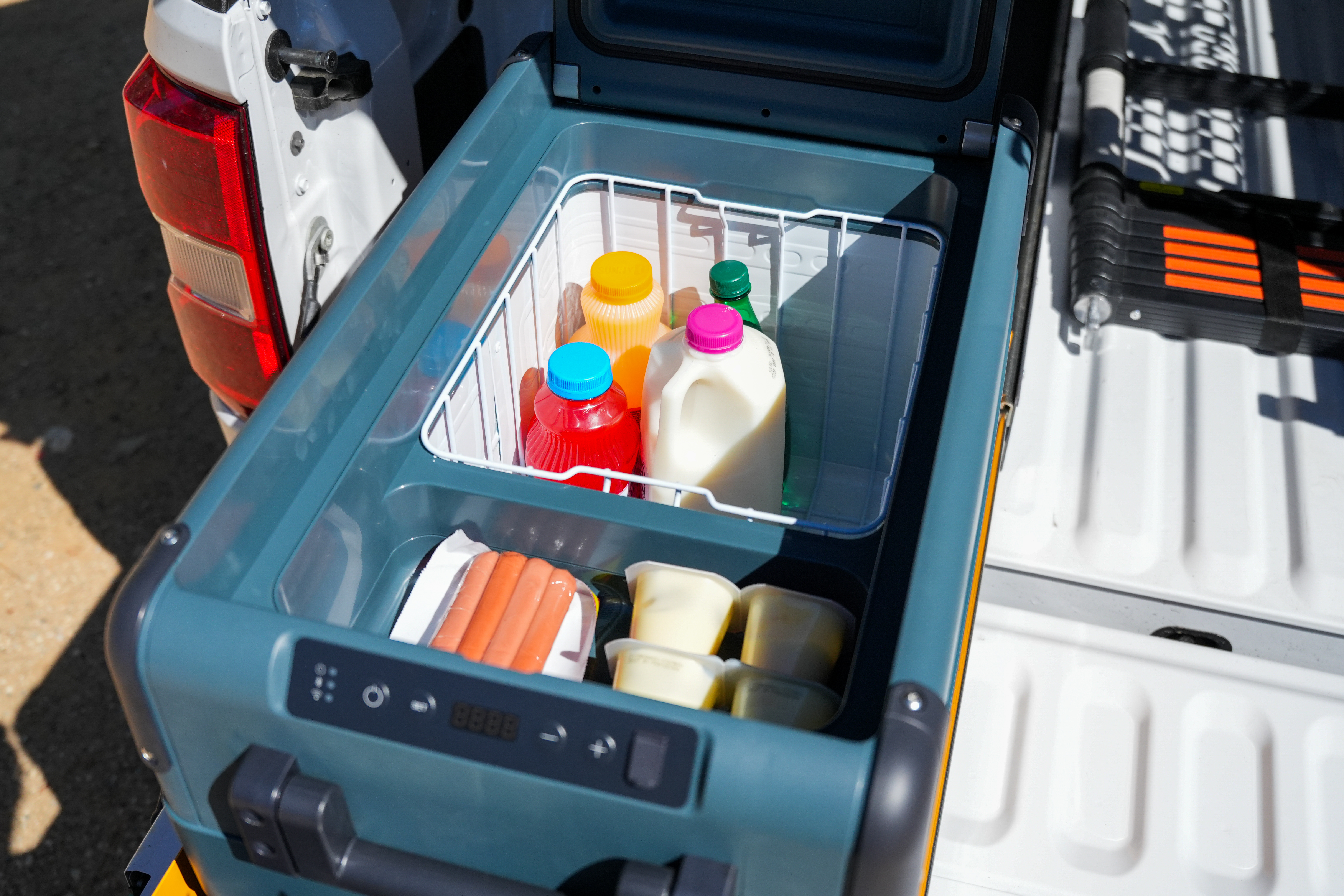 Portable fridge in a camper van loaded with milk, juice bottles, packaged food, and yogurt cups.