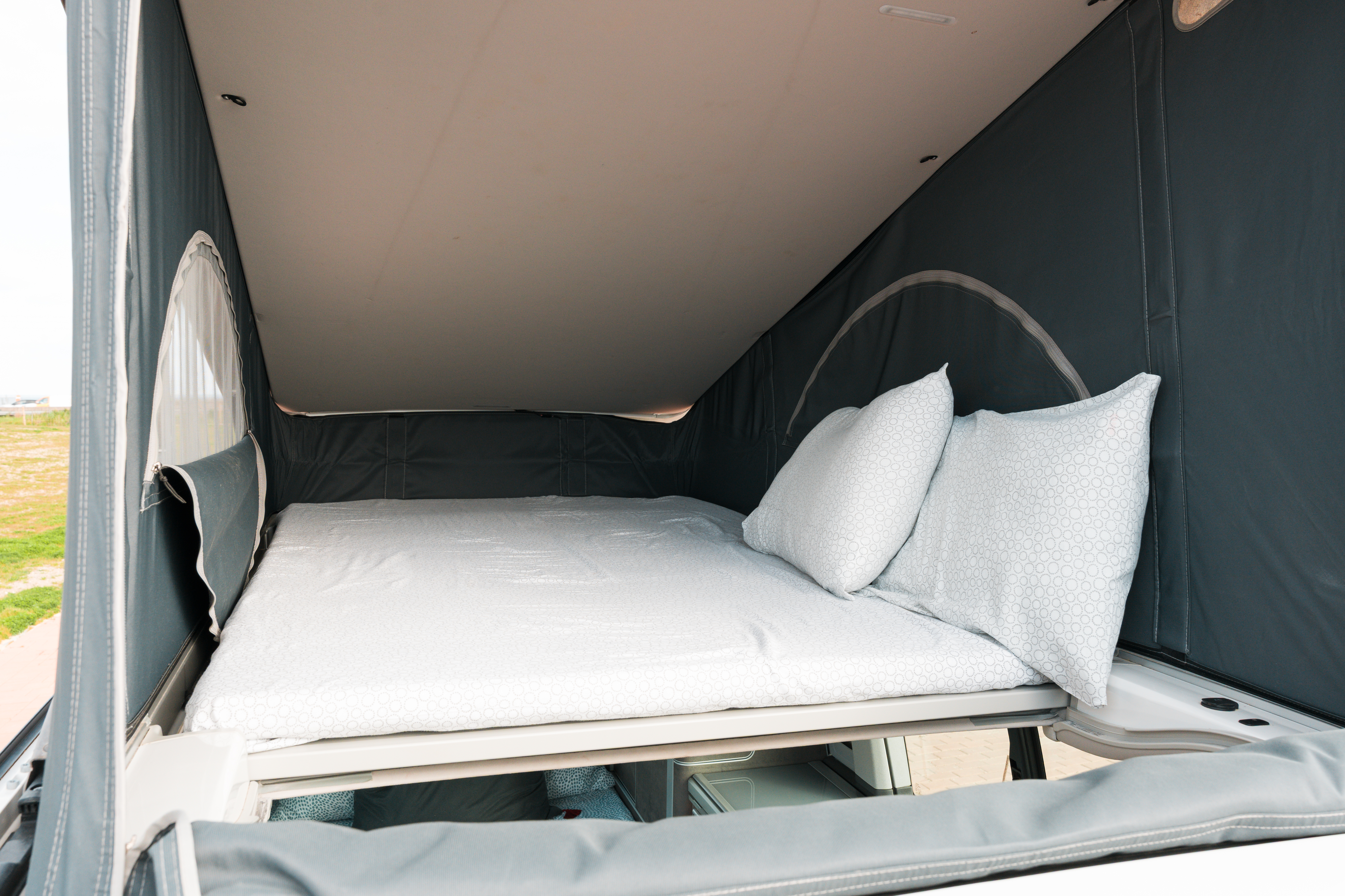 Interior view of a camper van pop-top roof bed with white bedding and two pillows, ready for use.