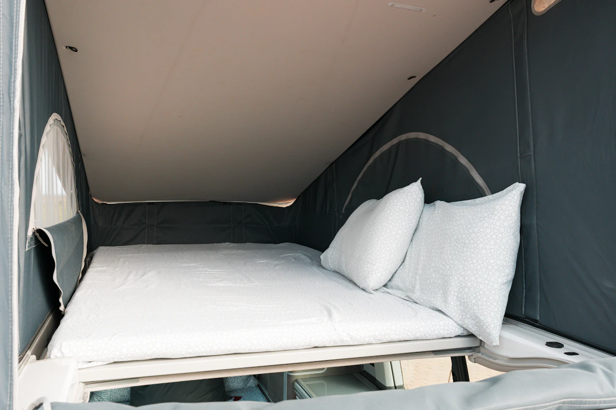 Interior view of a camper van pop-top roof bed with white bedding and two pillows, ready for use.