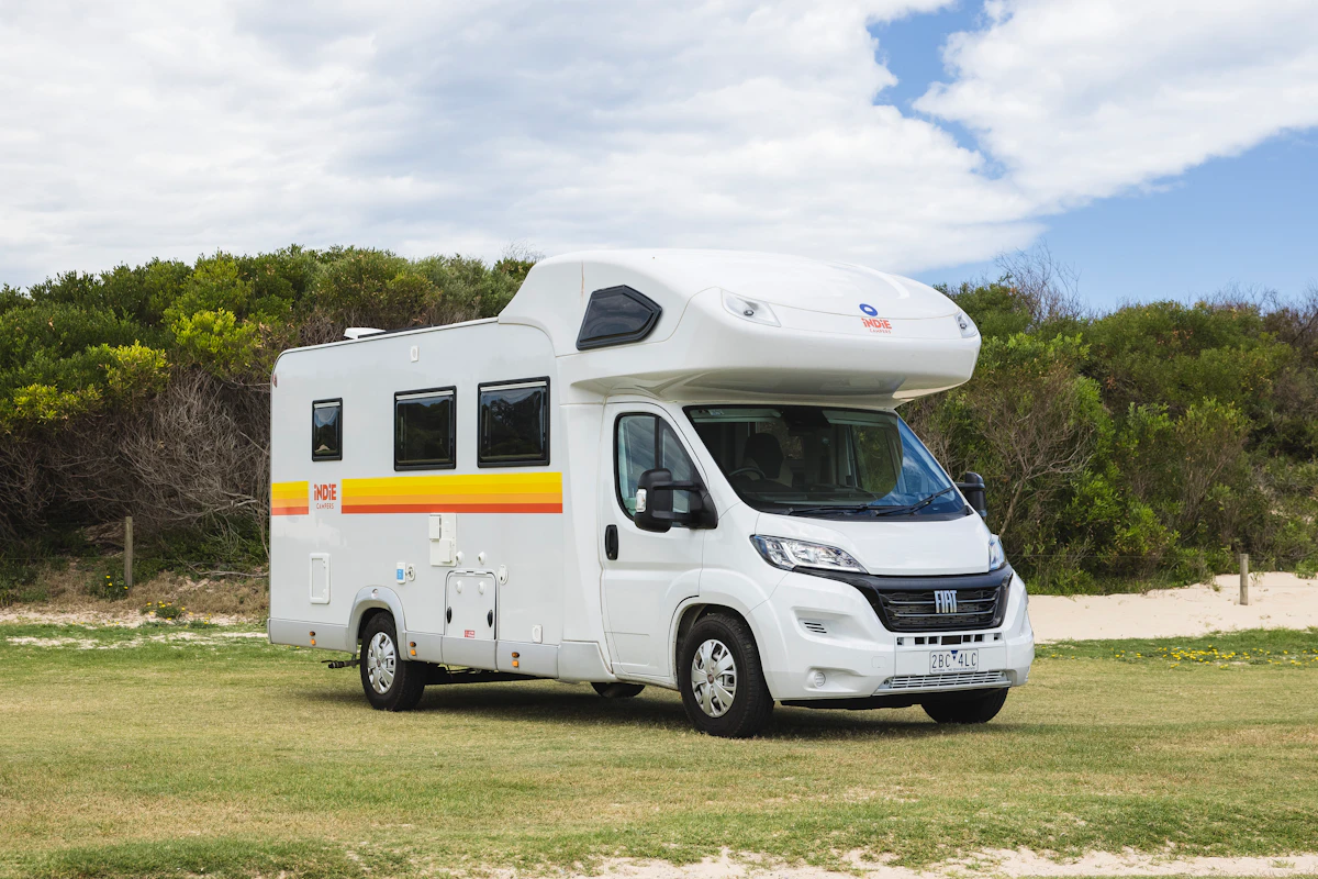 White campervan parked on grass with trees in the background under a partly cloudy sky.