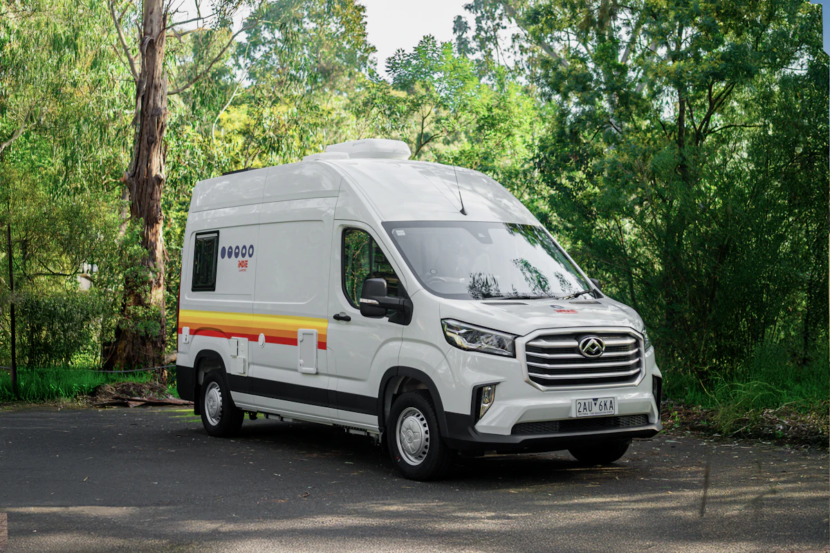 White campervan with yellow and red stripes parked outdoors near trees, suitable for road trips and camping adventures.