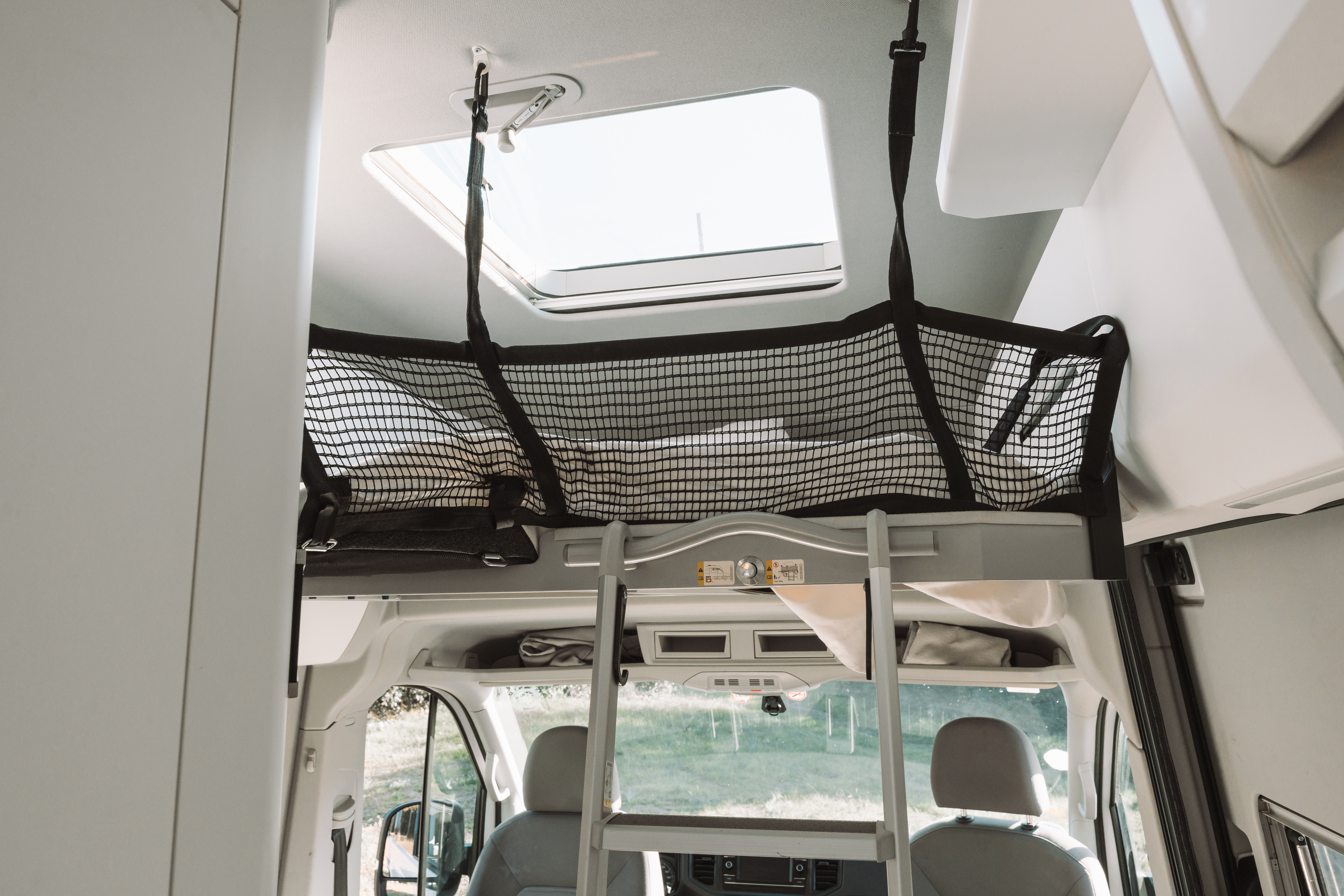 Van interior with loft bed, safety net, ladder, skylight, front seats, and cabinets visible.
