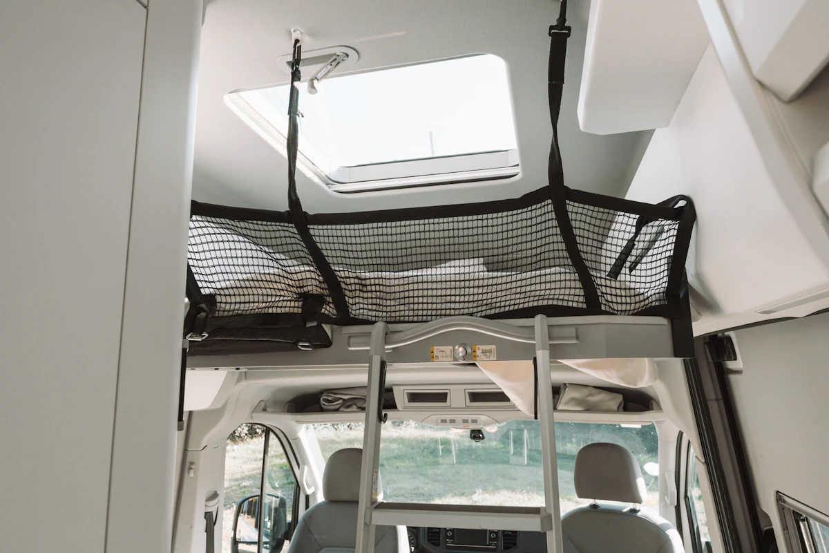 Van interior with loft bed, safety net, ladder, skylight, front seats, and cabinets visible.
