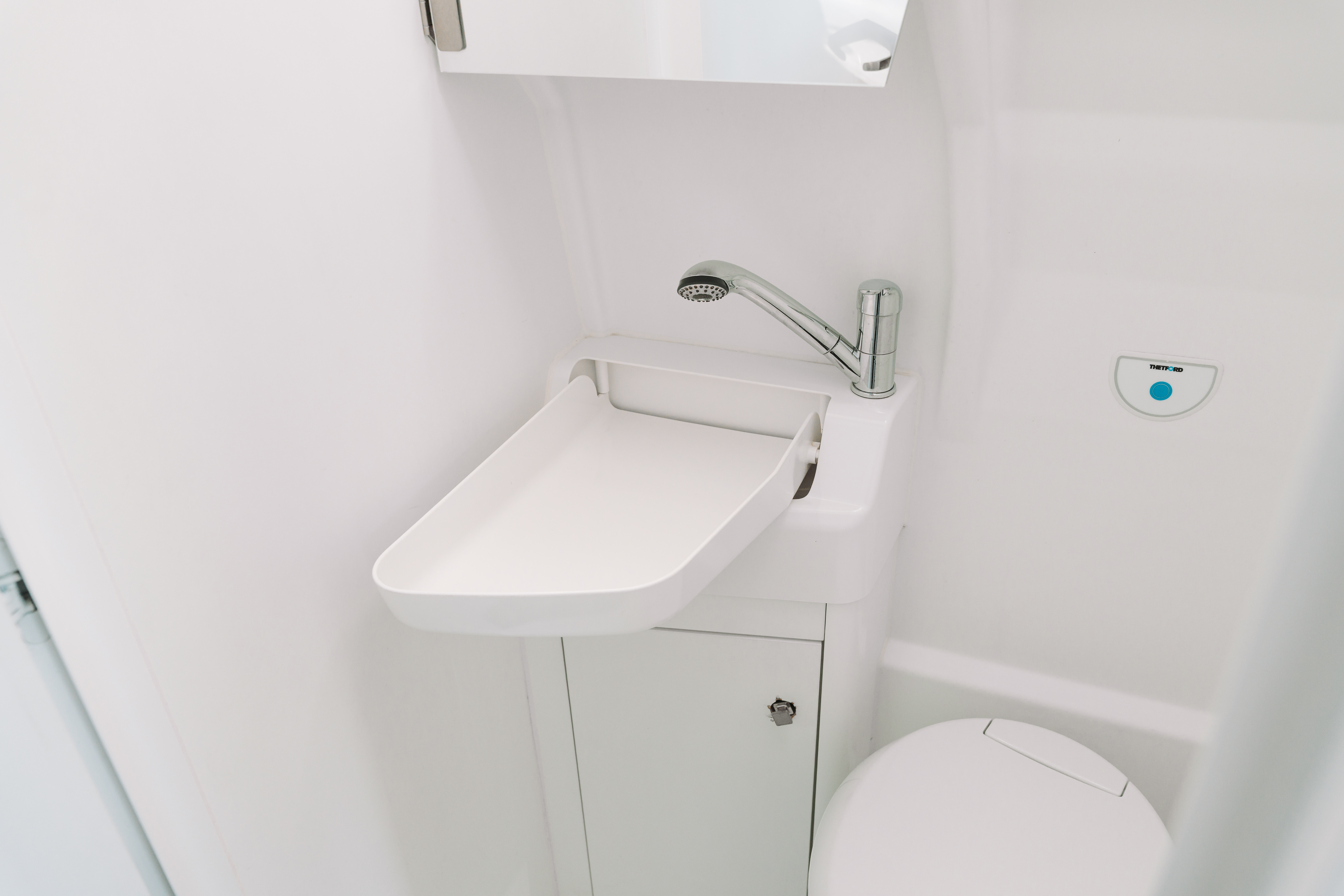 Compact van bathroom interior with white sink, faucet, under-sink cabinet, and toilet visible.