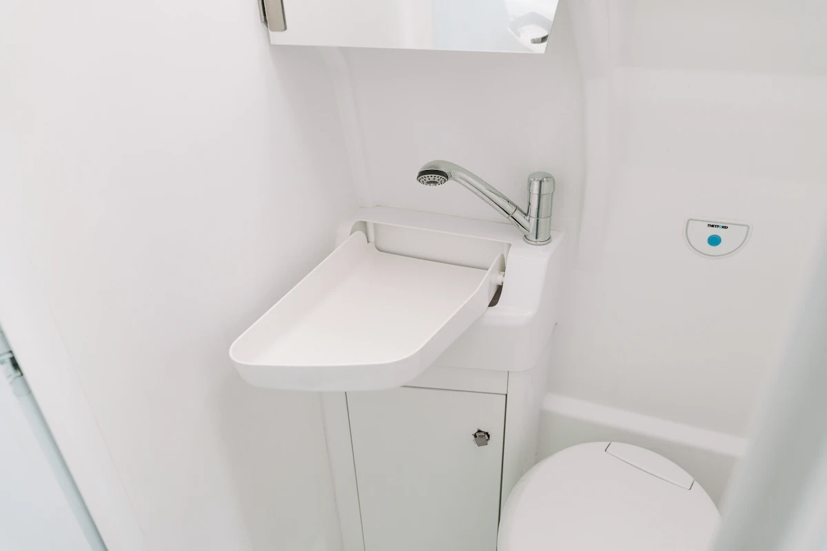 Compact van bathroom interior with white sink, faucet, under-sink cabinet, and toilet visible.