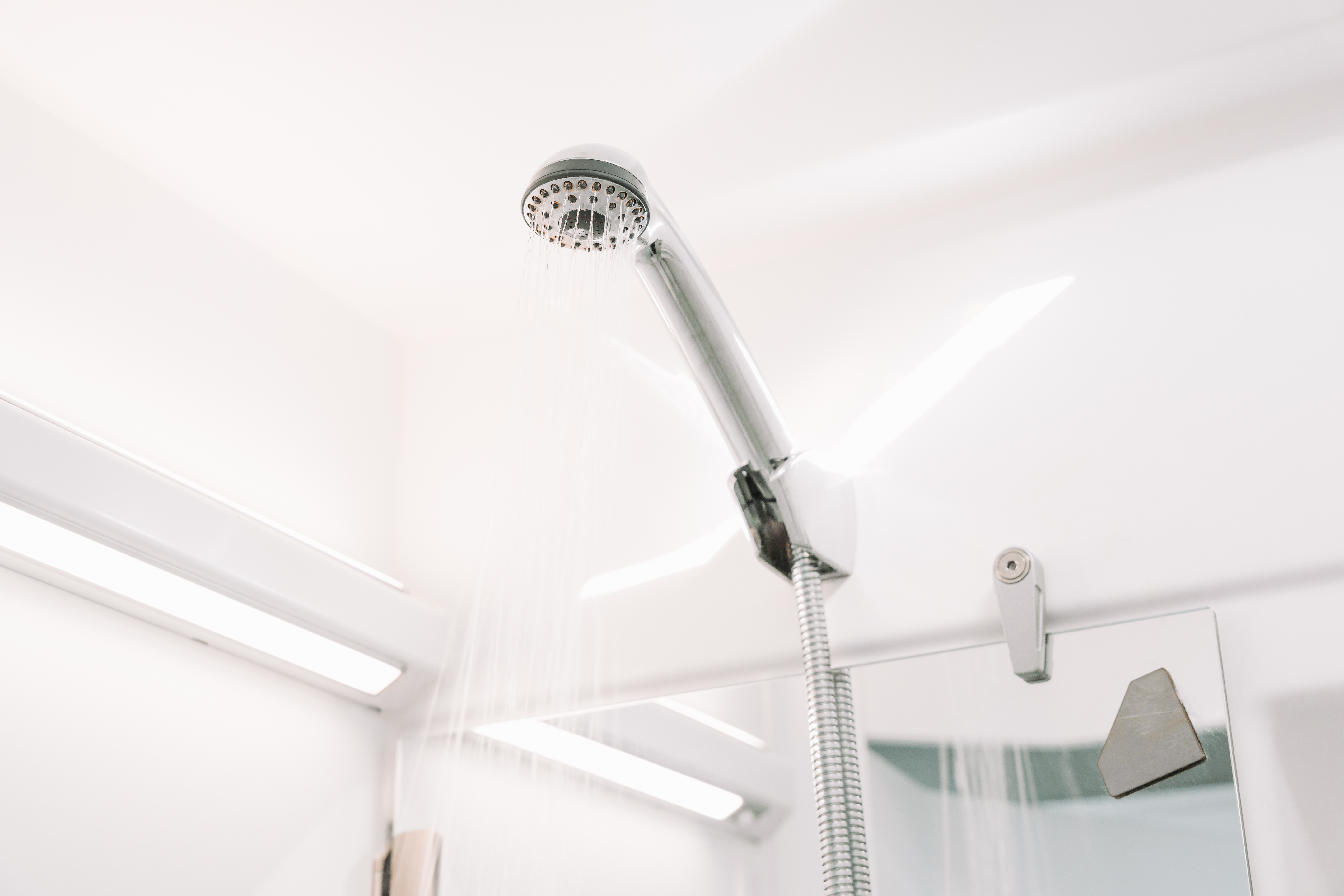 Showerhead with water flowing in compact, white van bathroom interior with mirror and ceiling lights.