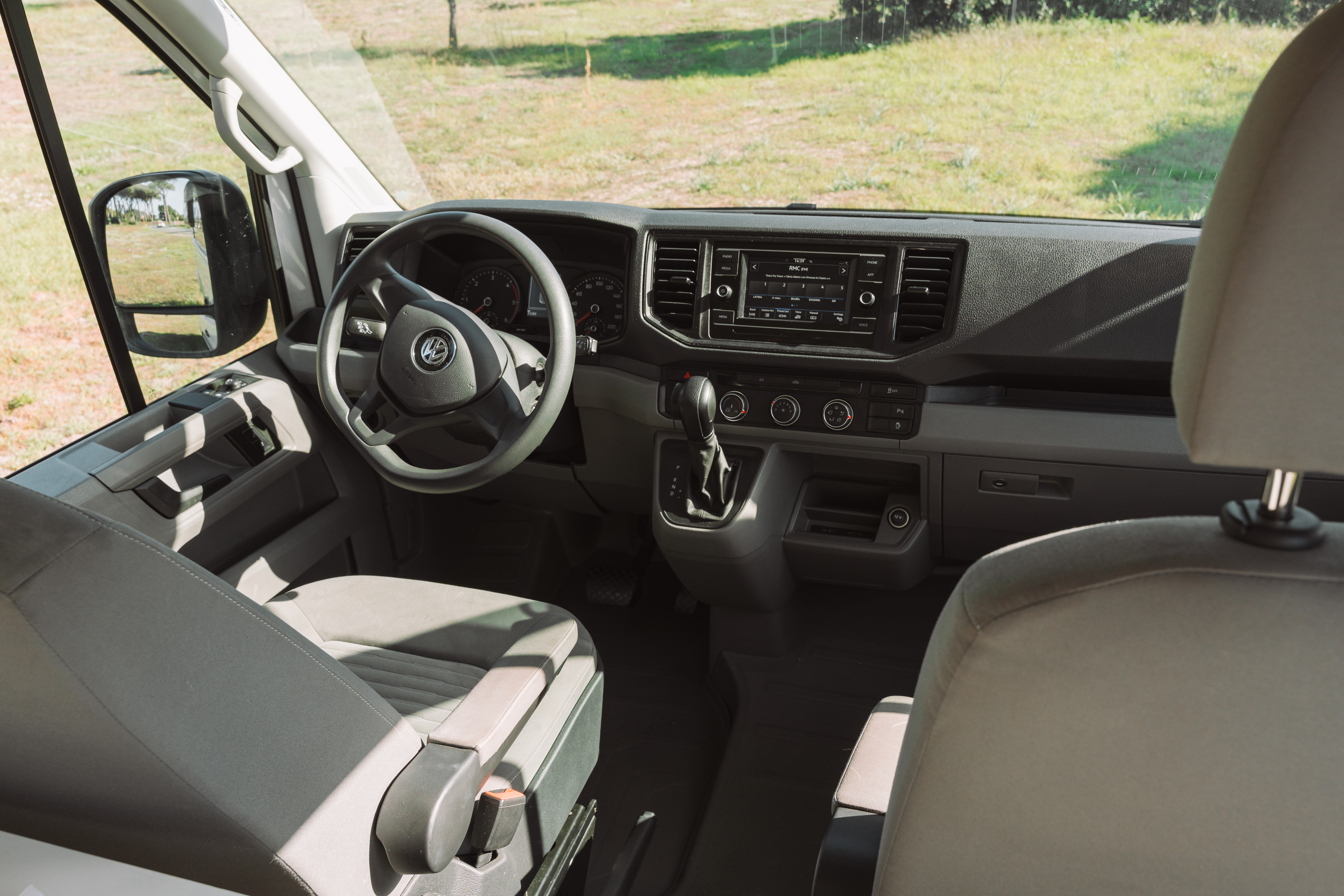 Driver cabin with two seats, steering wheel, dashboard, gear shift, and central control panel visible.