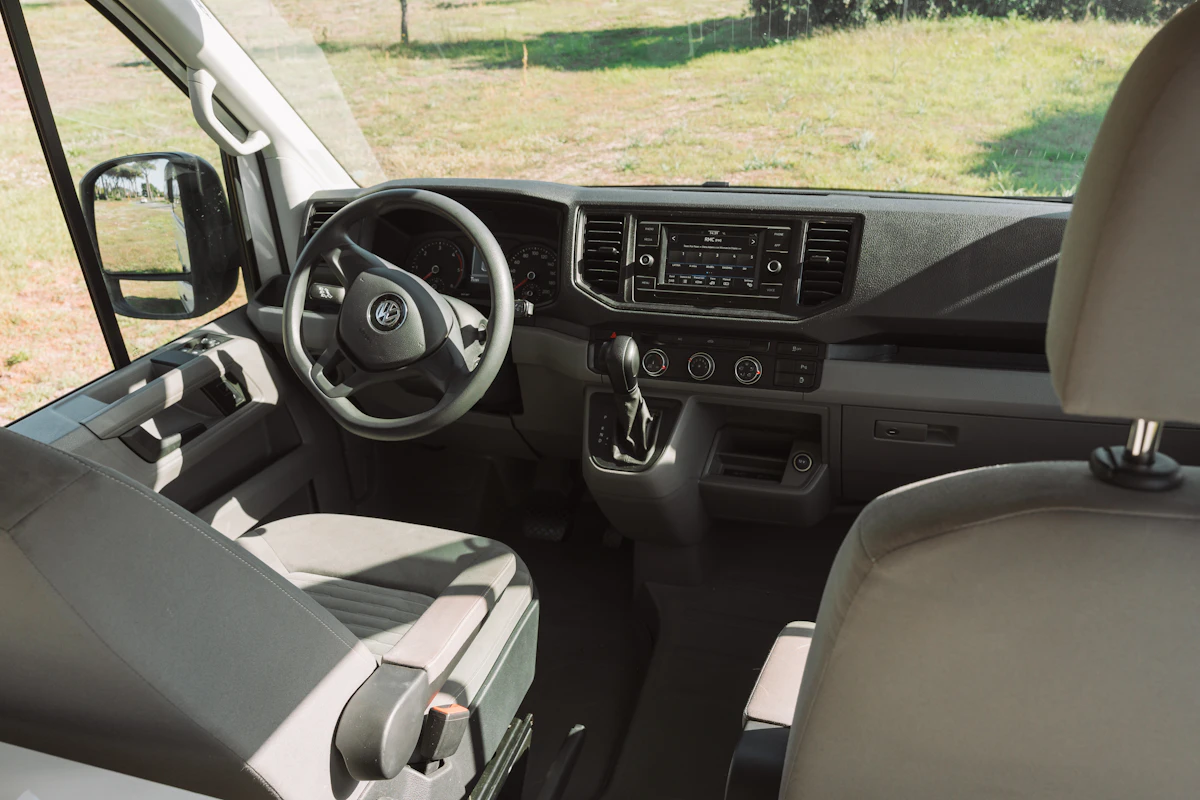 Driver cabin with two seats, steering wheel, dashboard, gear shift, and central control panel visible.