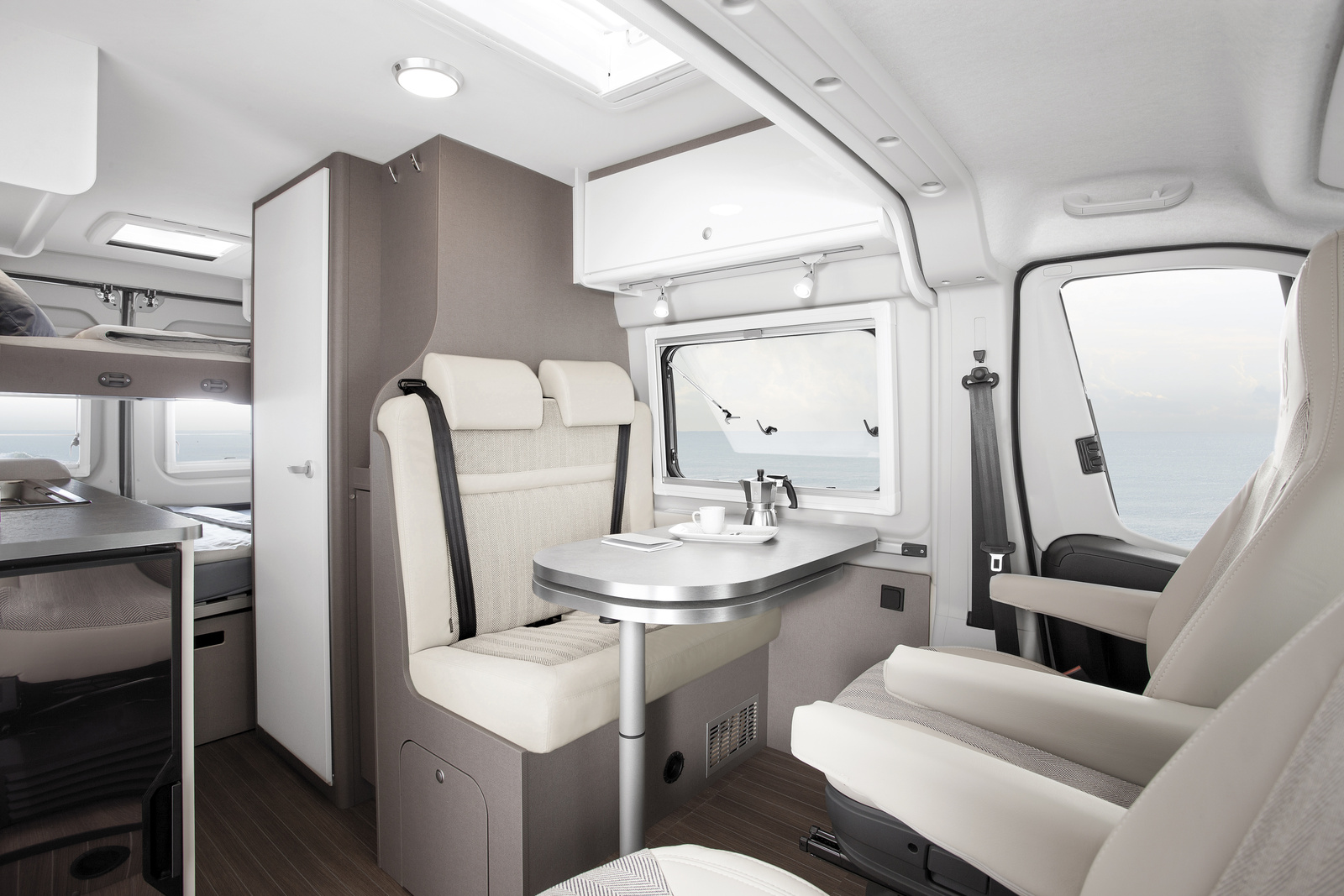 Two-seat bench, table, and two swivel chairs inside a van with overhead storage and window.