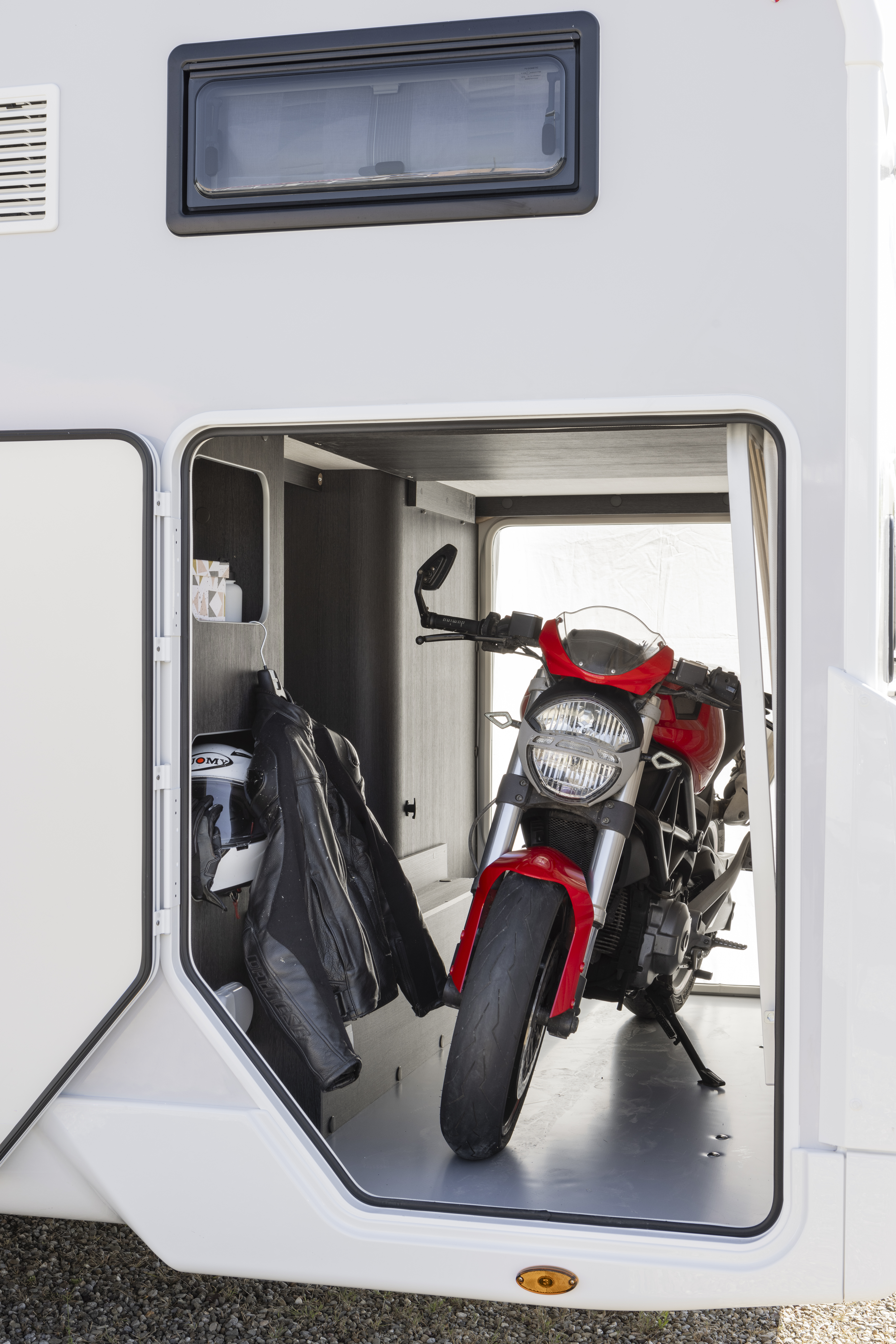 Van interior with motorcycle storage area, shelves, black cabinet, and hanging motorcycle jacket.
