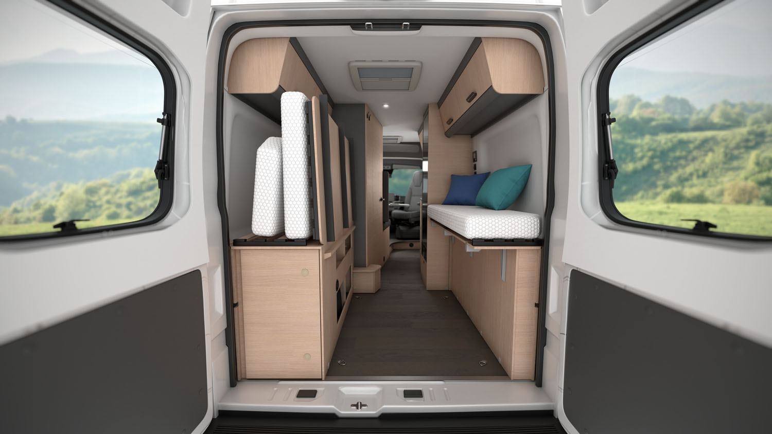 Rear view of van interior with bed, storage cabinets, shelves, and cushions, light wood and gray color scheme.