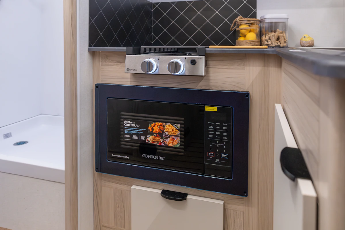 Compact van kitchen interior with built-in microwave, gas stove, and storage drawers visible.