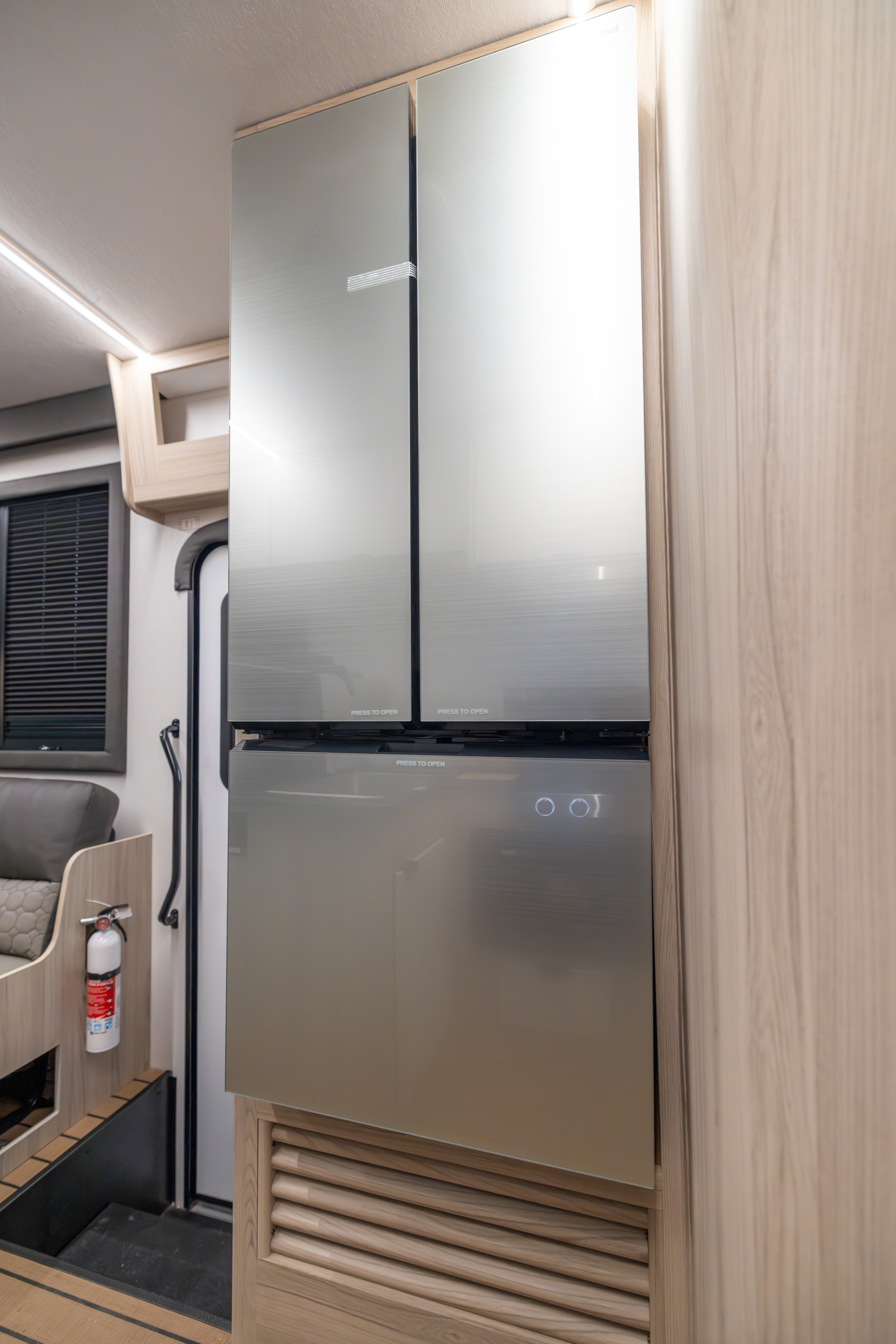 Van interior with large double-door fridge, wood paneling, seating, and window visible.
