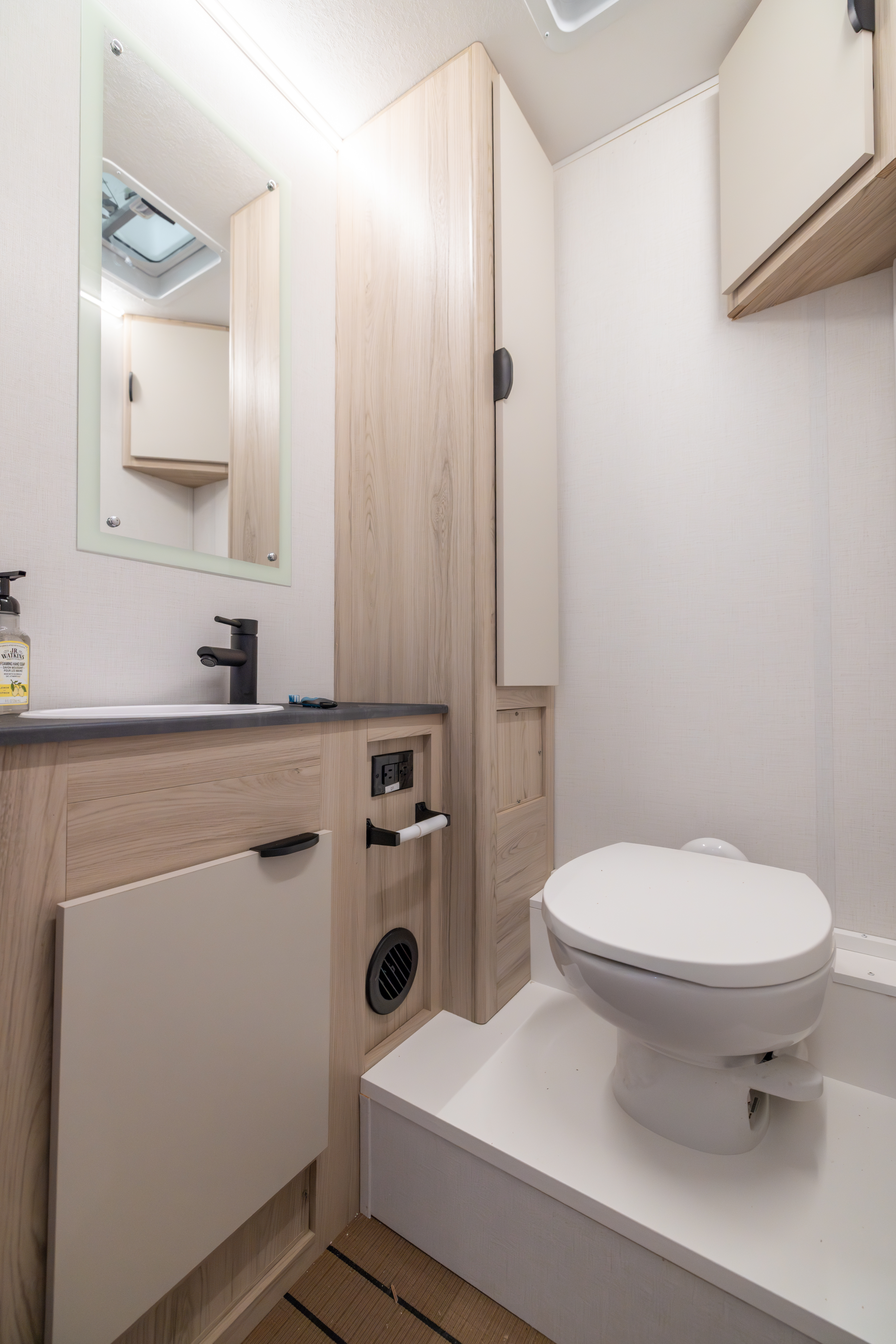 Compact van bathroom with toilet, sink, countertop, storage cabinet, and toilet paper holder visible in the interior.
