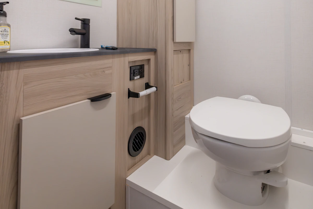 Compact van bathroom with toilet, sink, countertop, storage cabinet, and toilet paper holder visible in the interior.