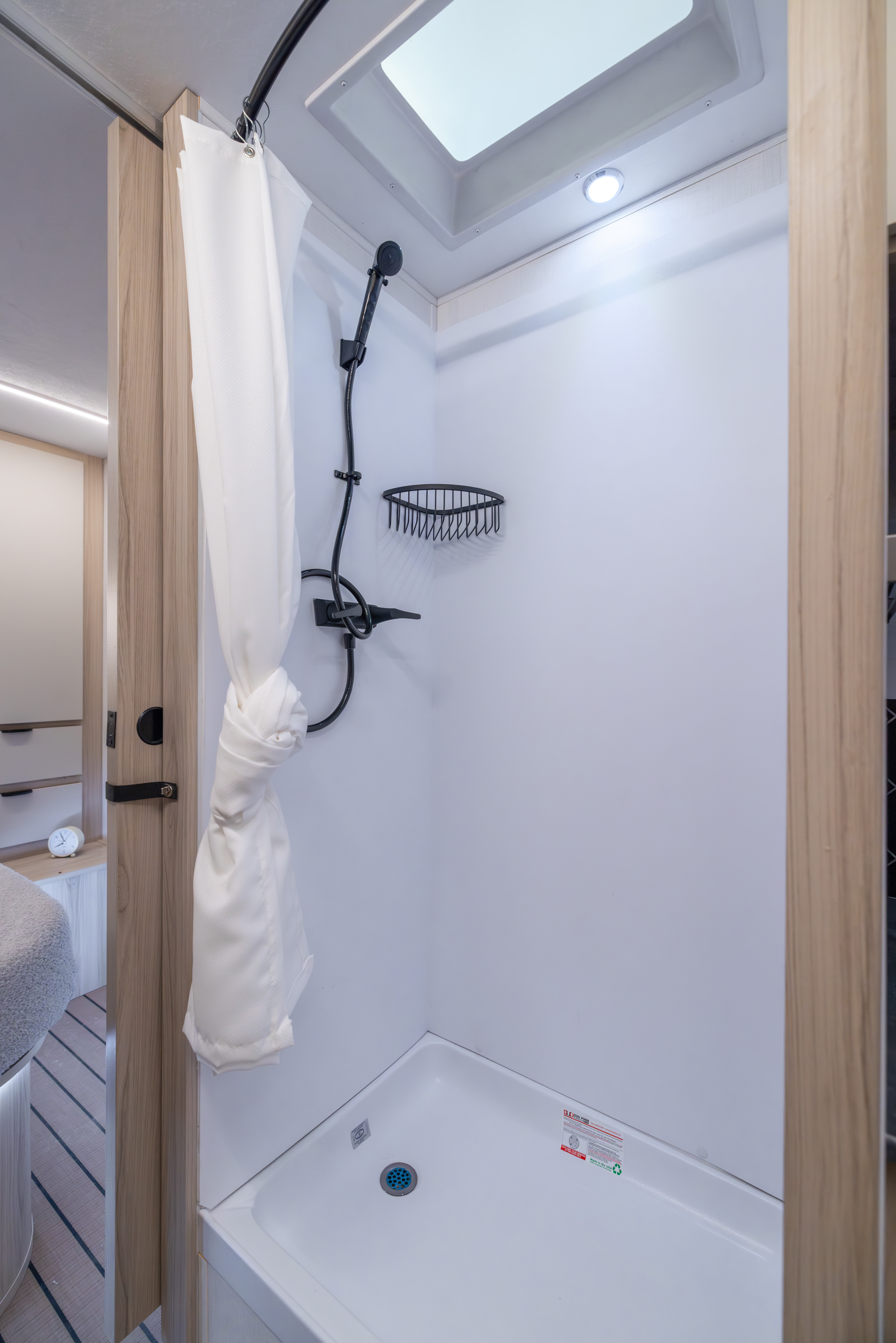 Van interior showing compact shower with curtain, black showerhead, soap basket, and overhead lighting.