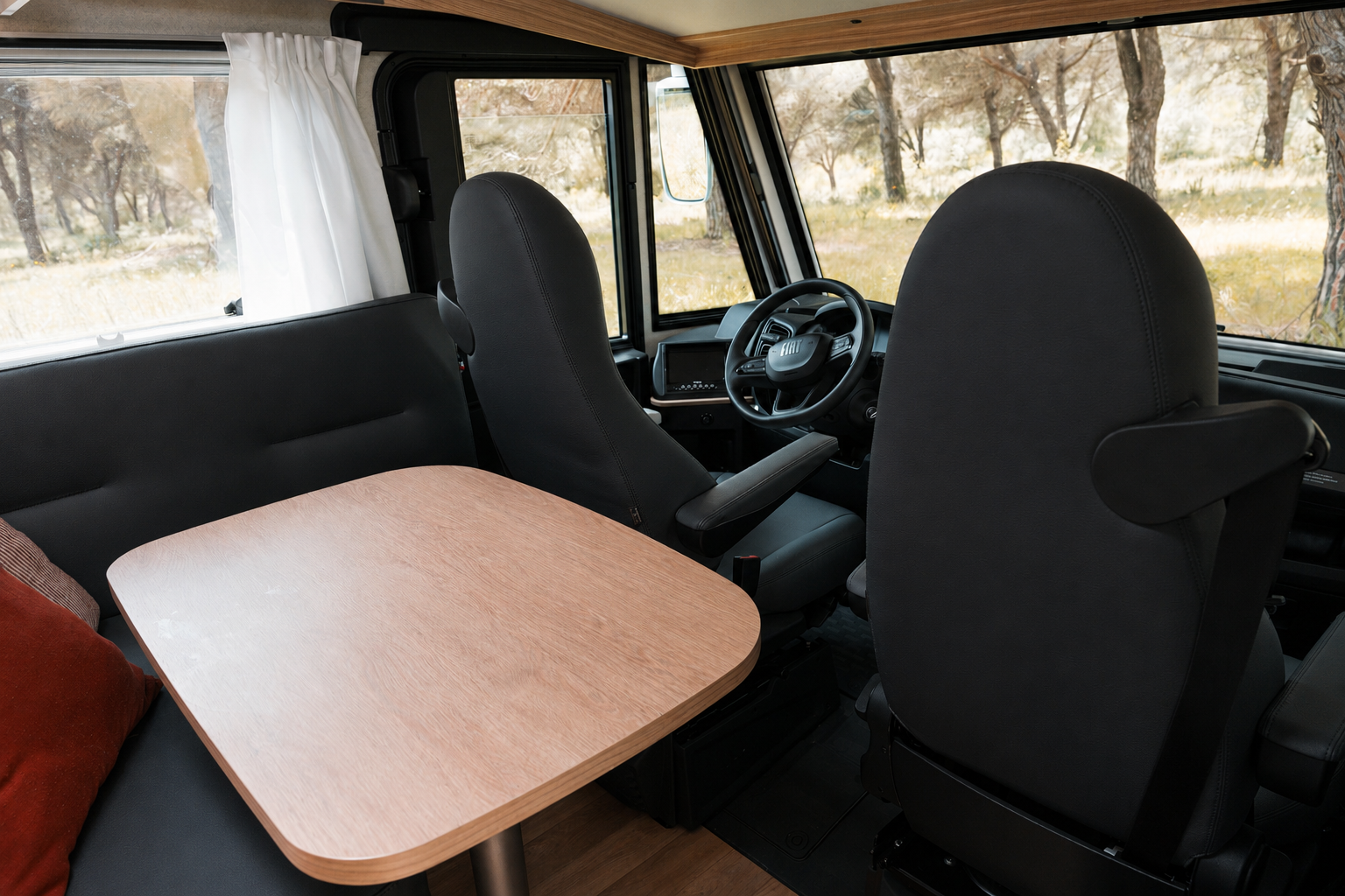 Van interior with front seats, a wooden table, side bench, and large windows with curtains.
