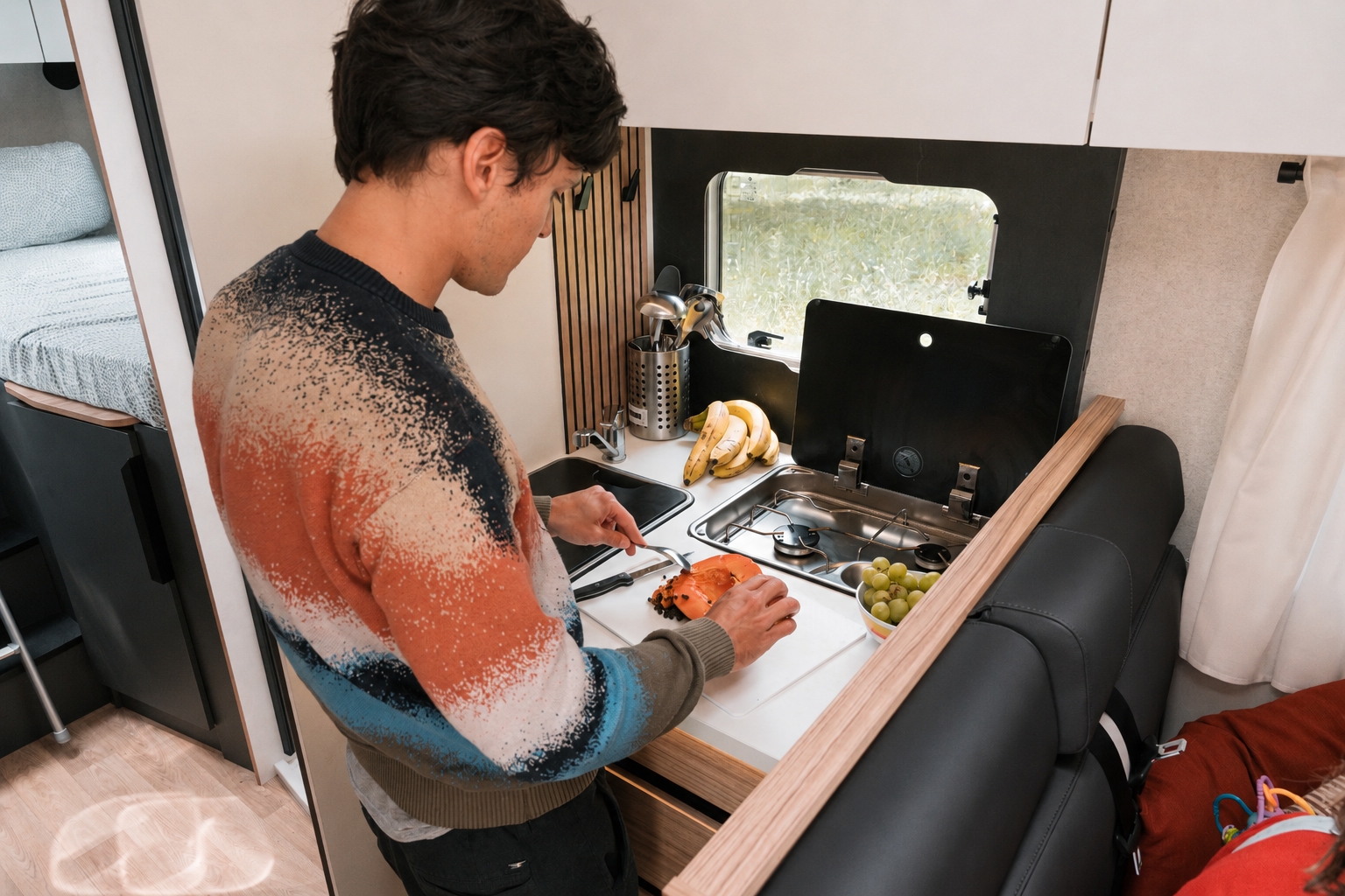 Compact van kitchen interior with sink, stove, overhead cabinets, countertop, and seating area visible.