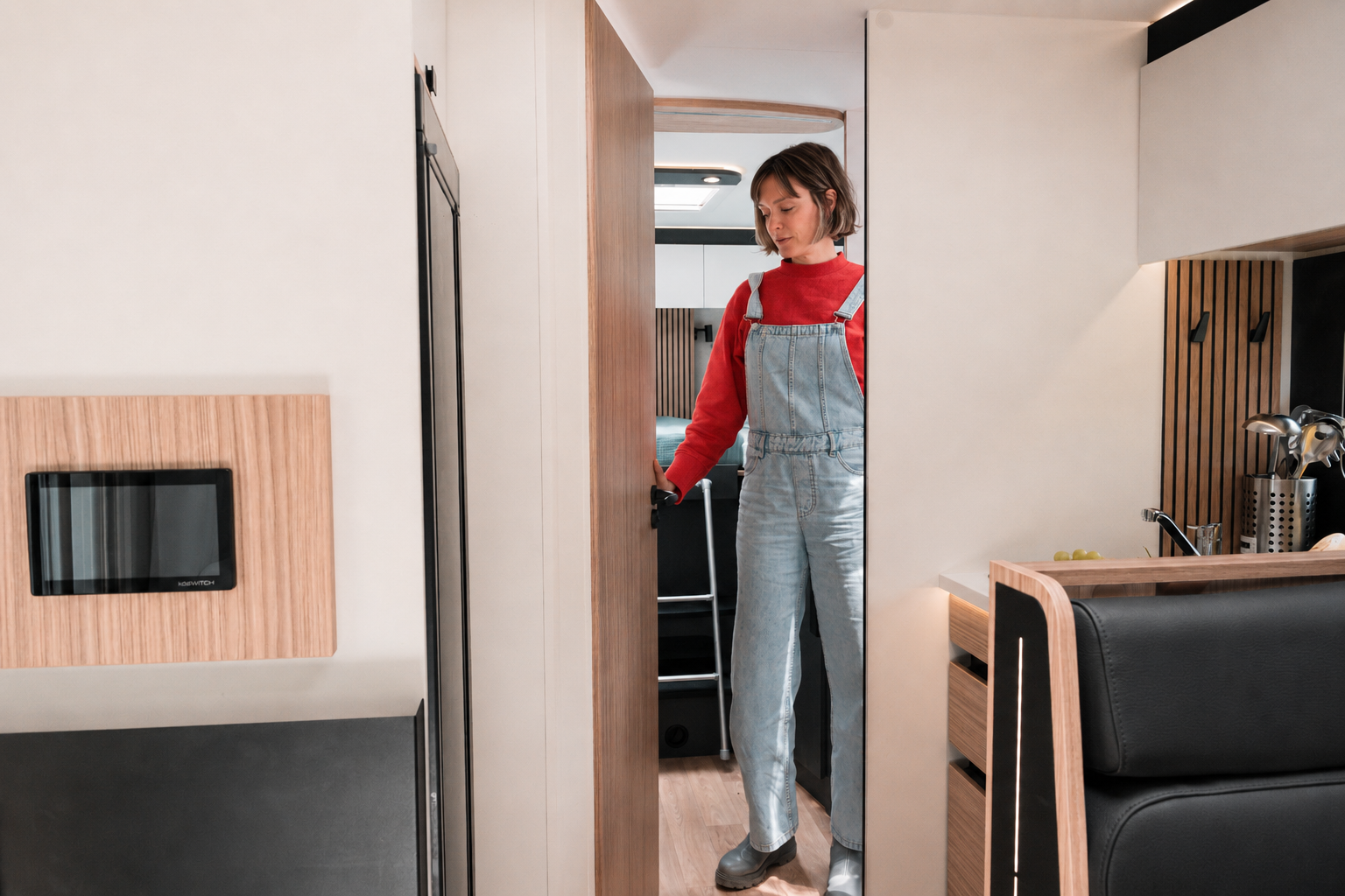 Van interior with vertical wood paneling, kitchen area, black seating, and built-in storage visible.