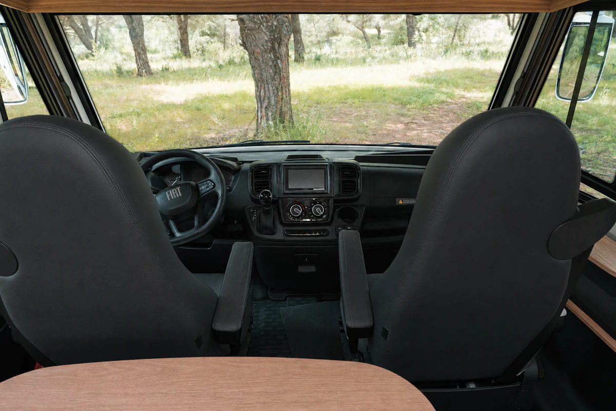 Front driver and passenger seats with dashboard, steering wheel, and wooden table visible inside the van.