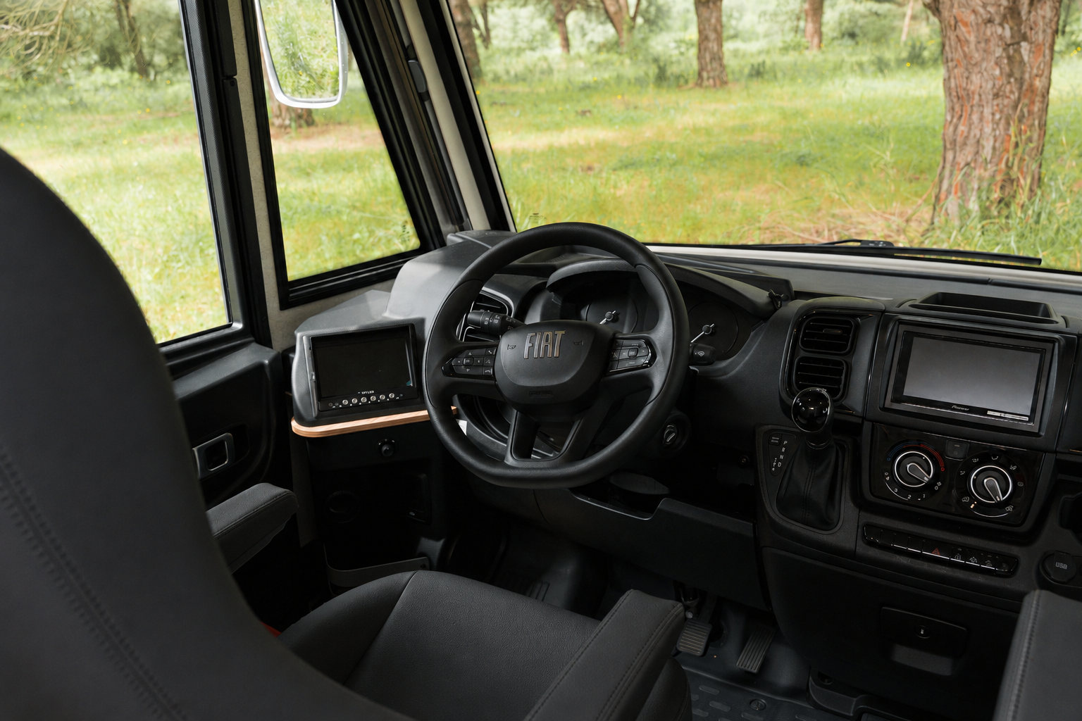 Driver cabin with steering wheel, dashboard, control panel, and two seats visible inside the van.