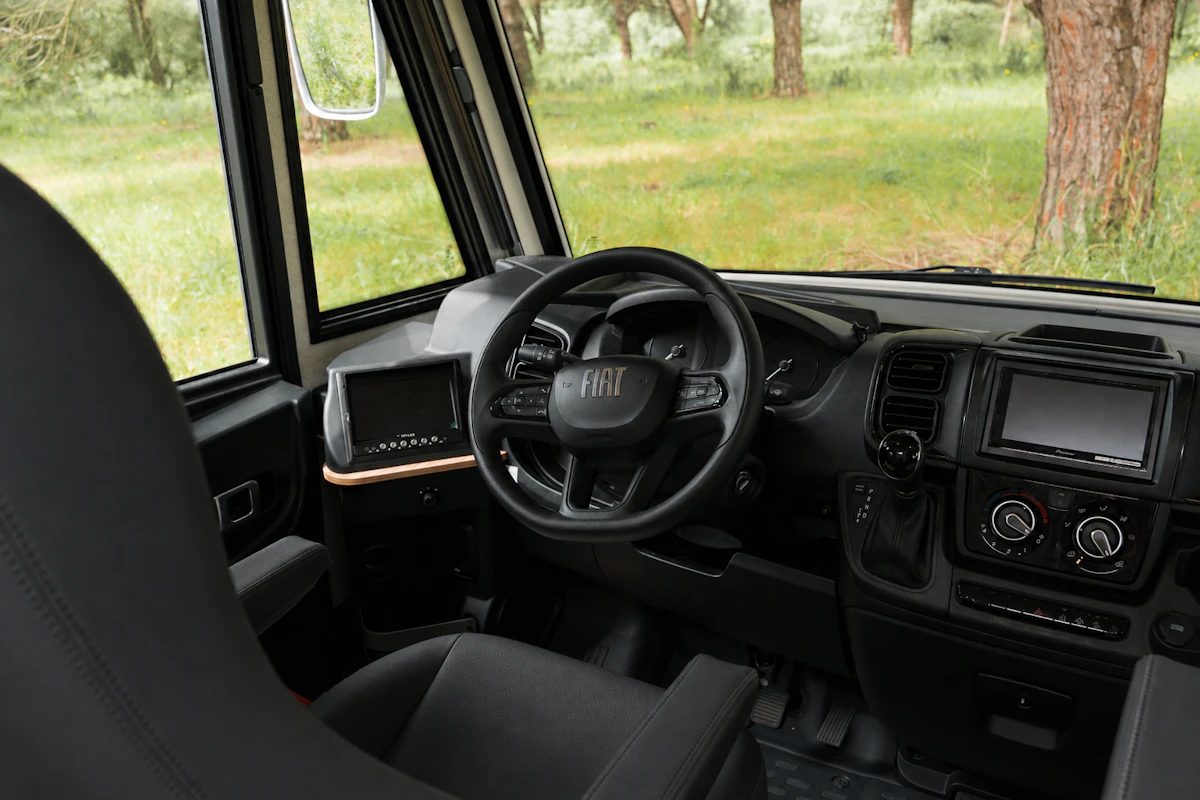 Driver cabin with steering wheel, dashboard, control panel, and two seats visible inside the van.