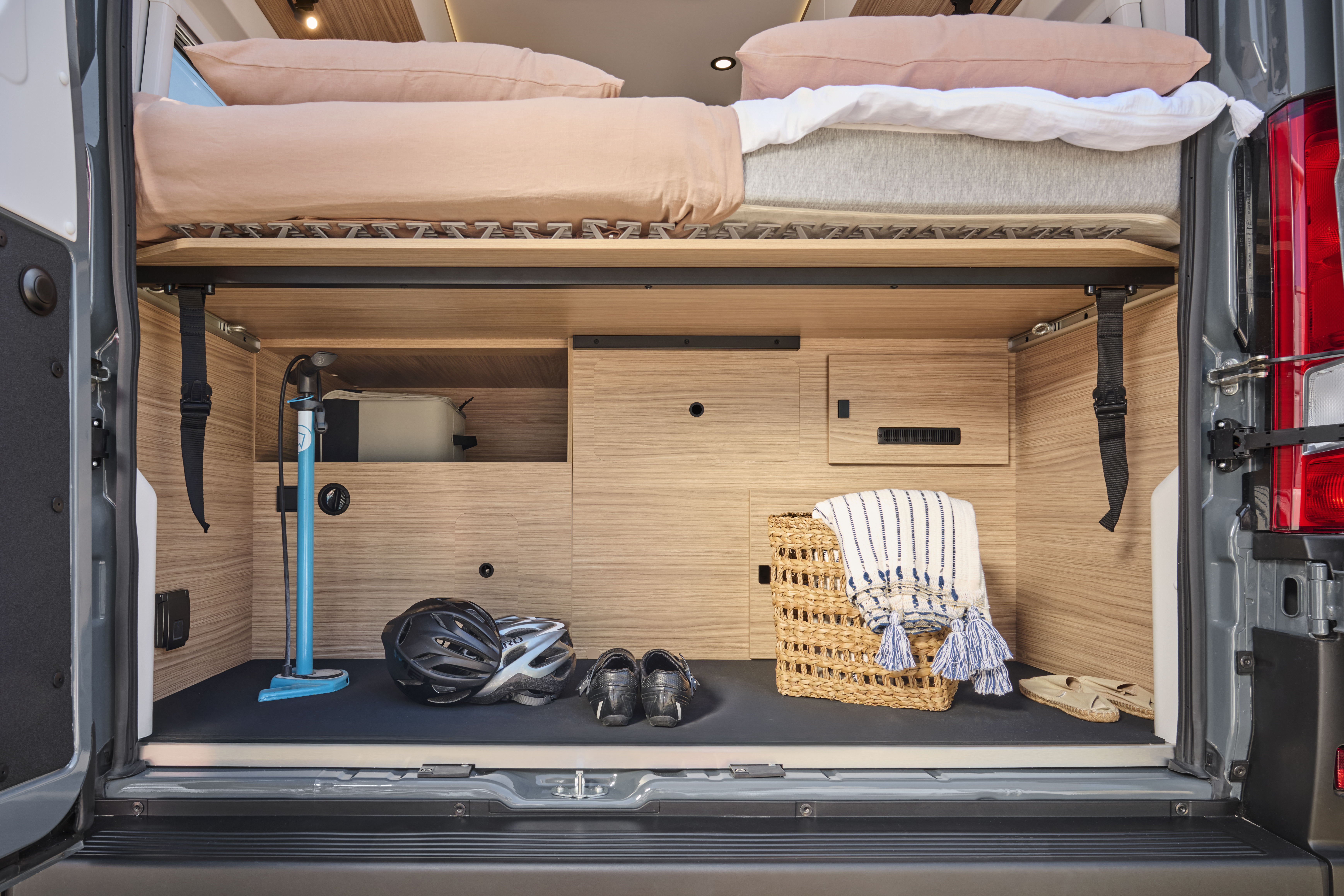 Rear interior view of van showing storage space, cabinets, bedding above, and various equipment.