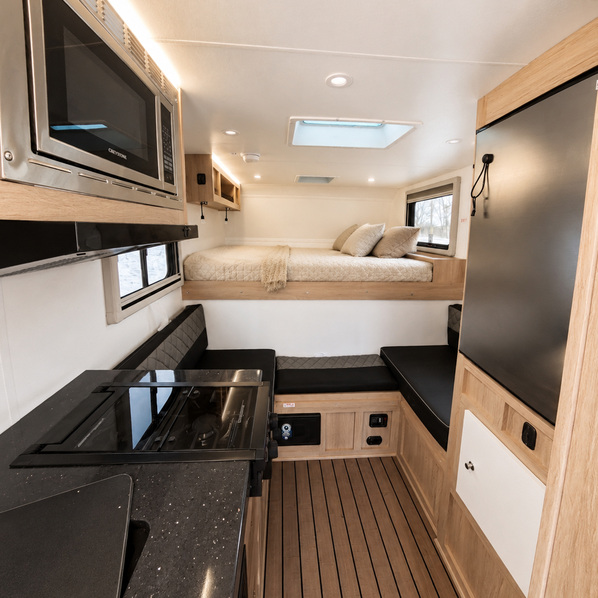 Compact van interior with built-in bed, microwave, stove, seating area, and wooden cabinetry visible.