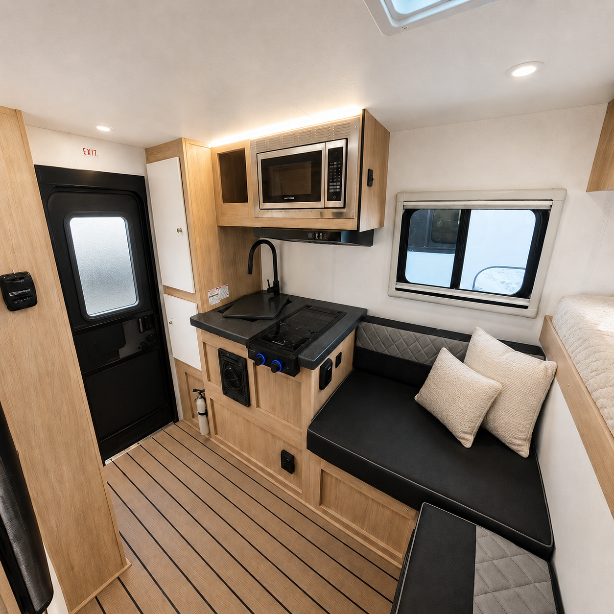 Van interior with compact kitchen, sink, microwave, bench seating with cushions, window, and entry door visible.