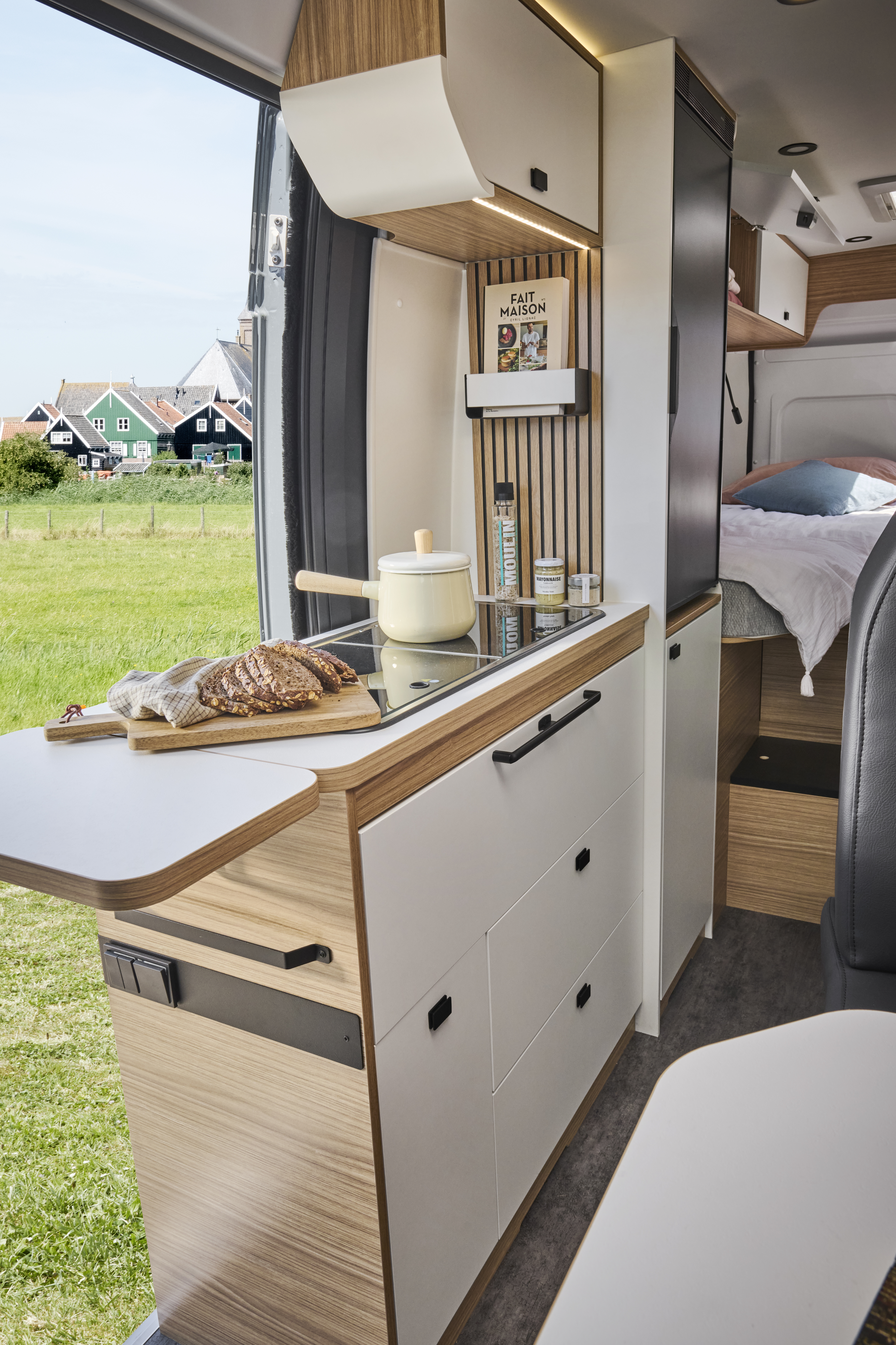 Compact van interior with kitchen counter, stove, cabinets, and a bed in the rear section.
