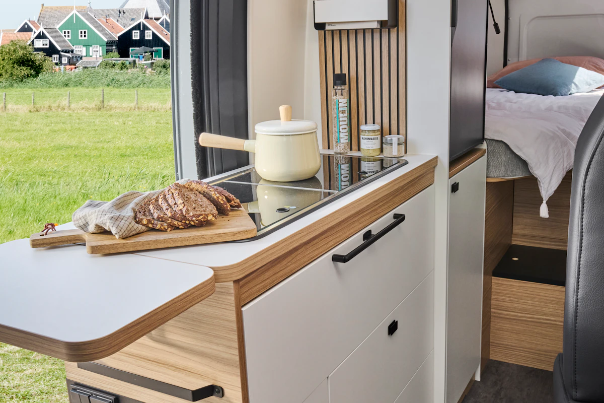 Compact van interior with kitchen counter, stove, cabinets, and a bed in the rear section.