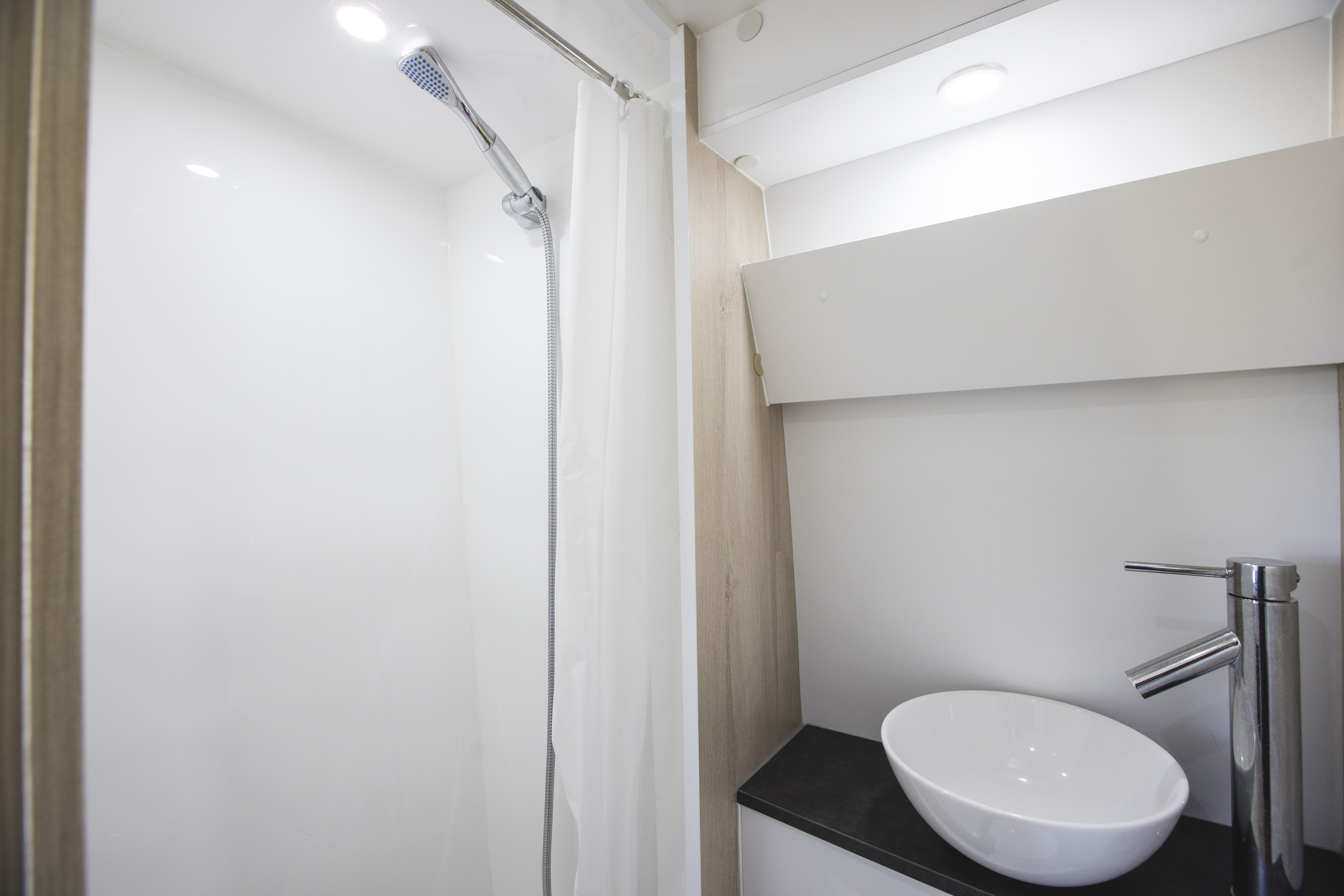 Van interior with shower, white sink, countertop, faucet, and overhead lighting visible.