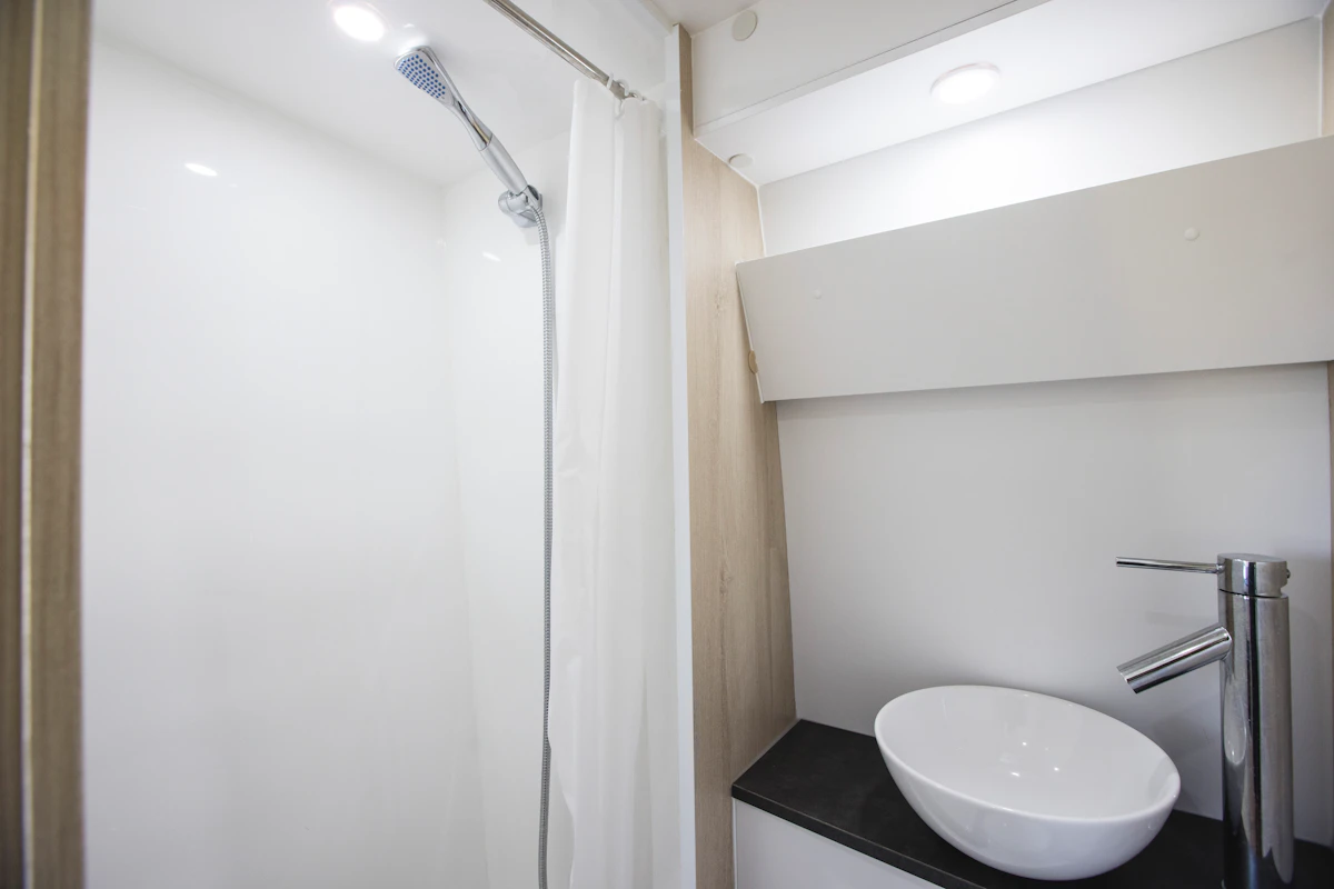 Van interior with shower, white sink, countertop, faucet, and overhead lighting visible.