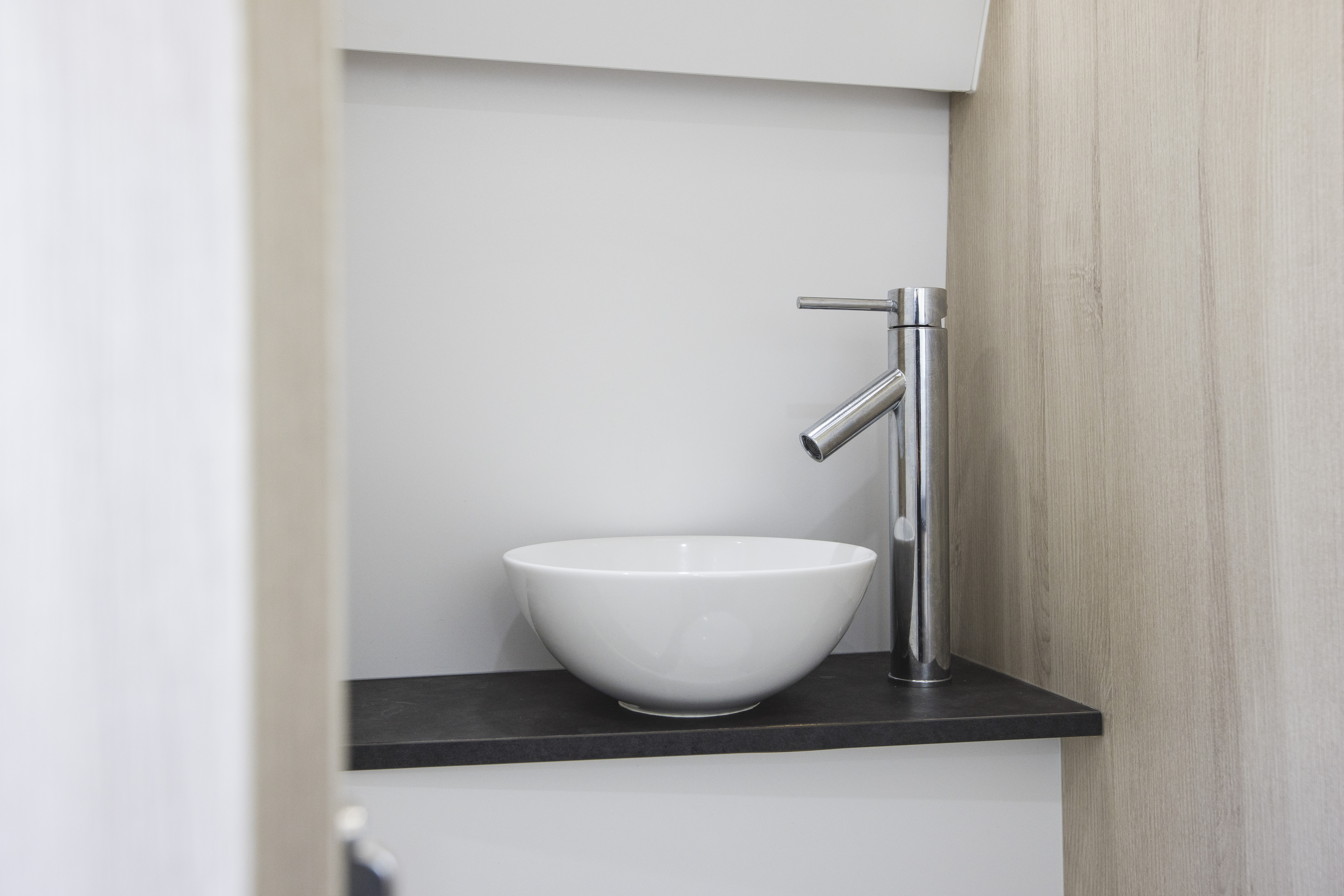 Compact van bathroom with round white sink and modern metal faucet on a black countertop.