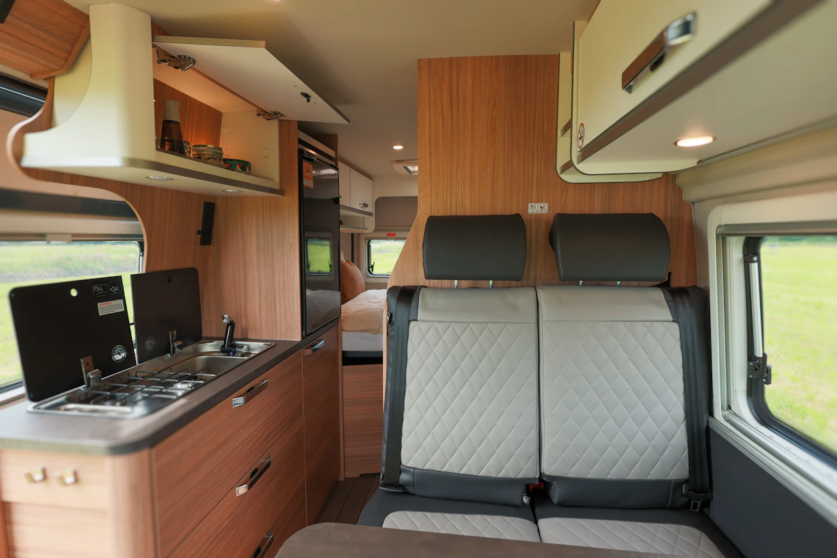 Modern camper van interior with dining table, cushioned bench, swivel seats, and window, designed for travel comfort.