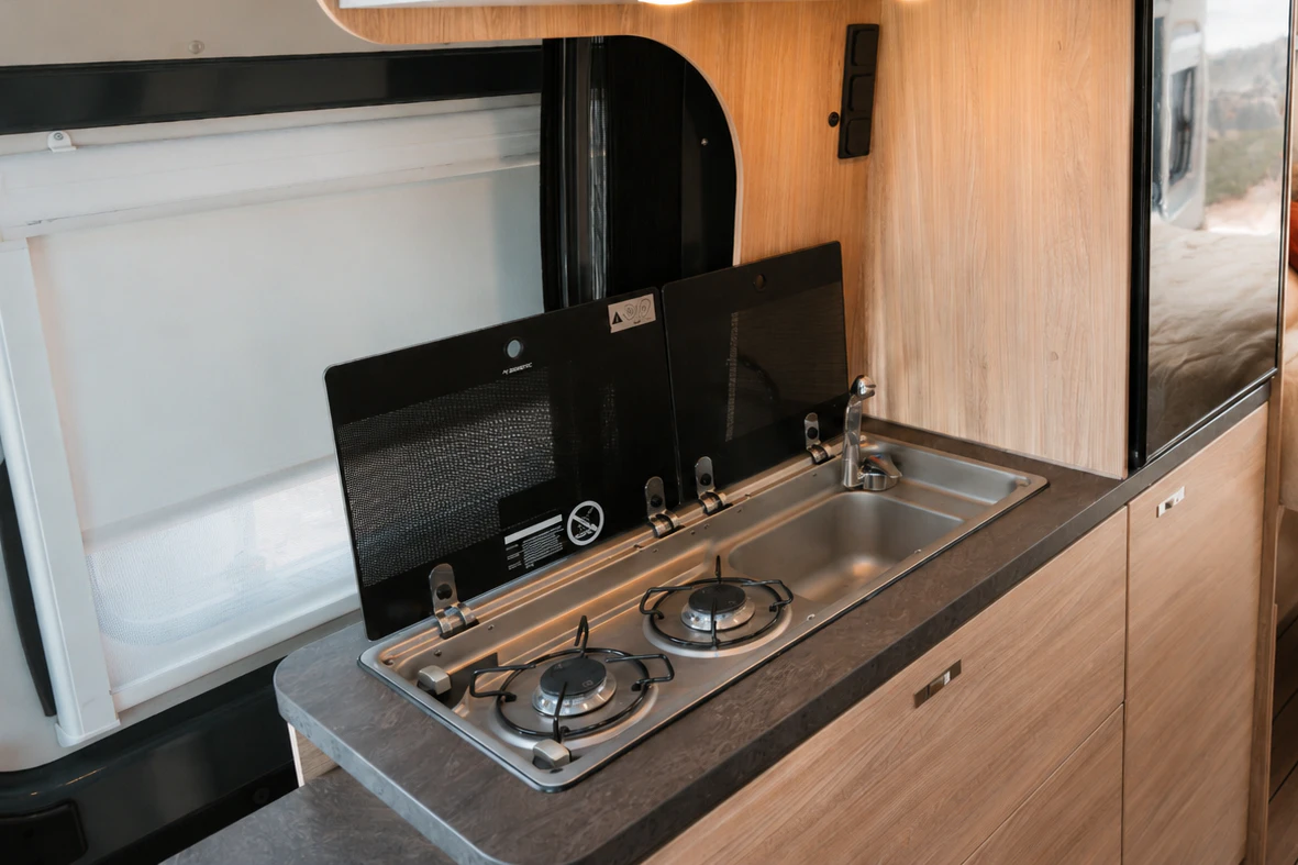 Cucina interna con fornelli a gas, lavello, frigorifero, pensili e letto sul retro del van.