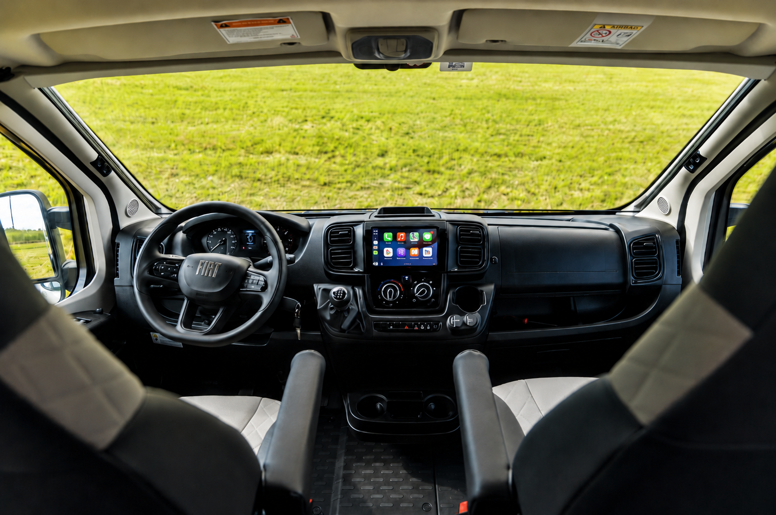 Front cockpit view showing dashboard, steering wheel, touchscreen display, two seats, and storage compartments.