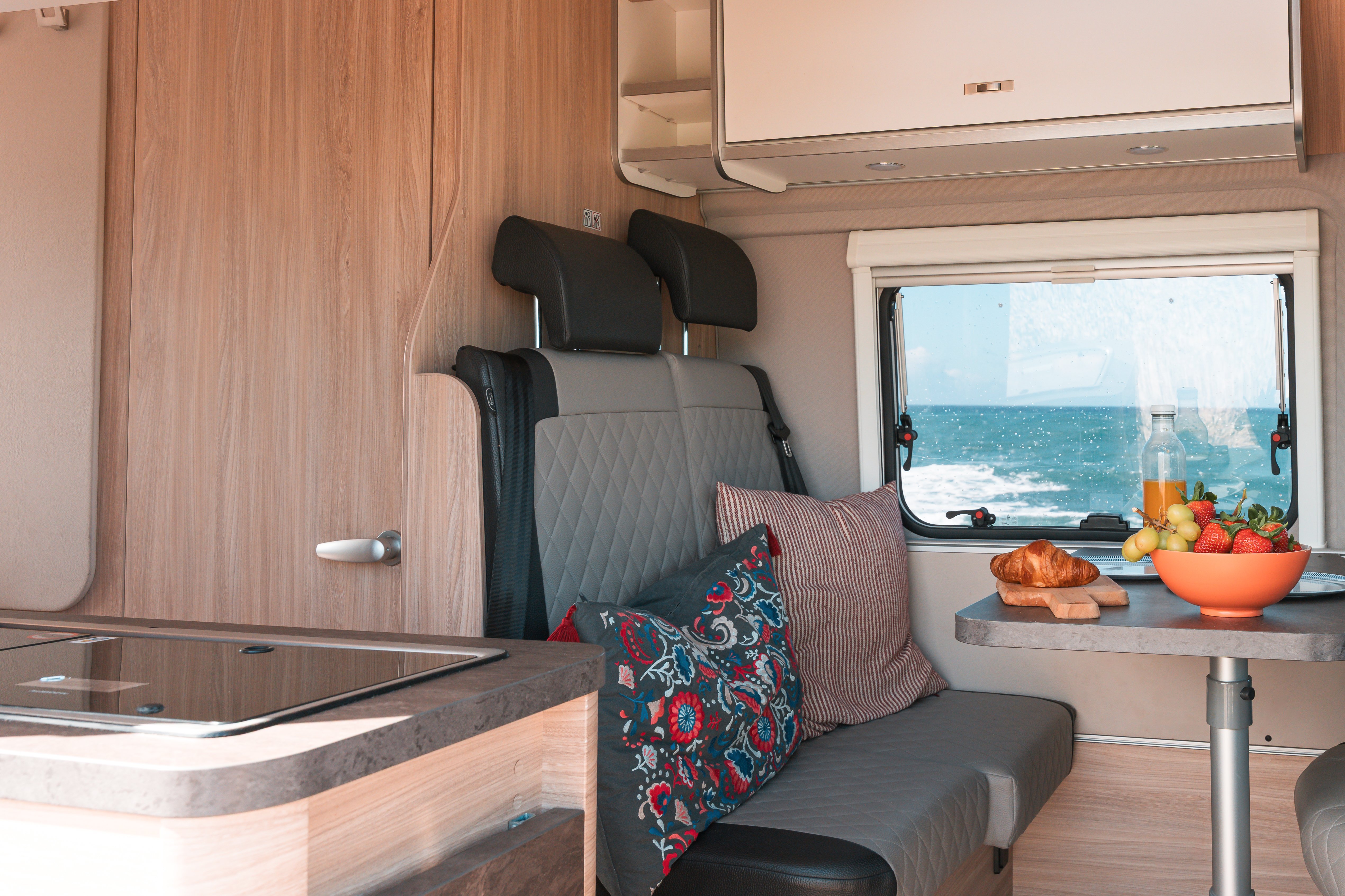 Van interior with dining table, two seats, cushions, countertop, and window, showing kitchen and seating area layout.
