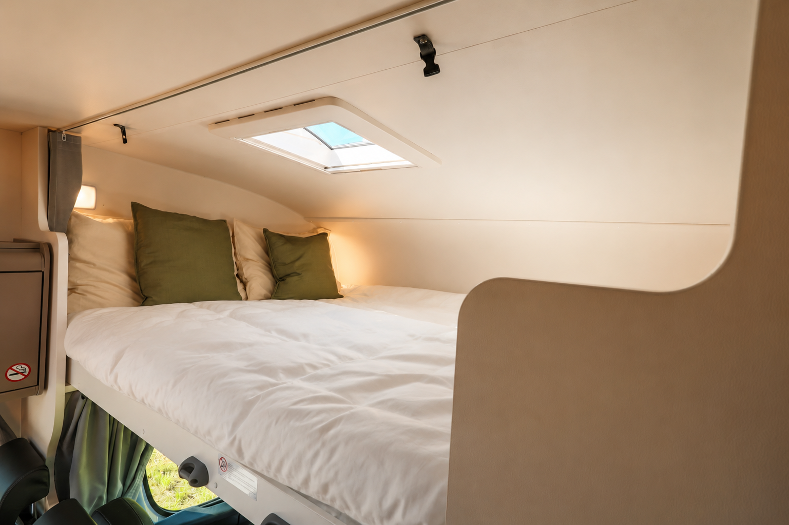 Raised bed area inside van with skylight, pillows, and overhead lighting.
