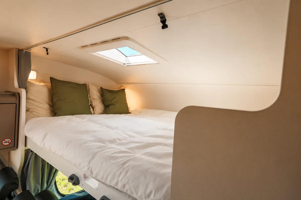 Raised bed area inside van with skylight, pillows, and overhead lighting.