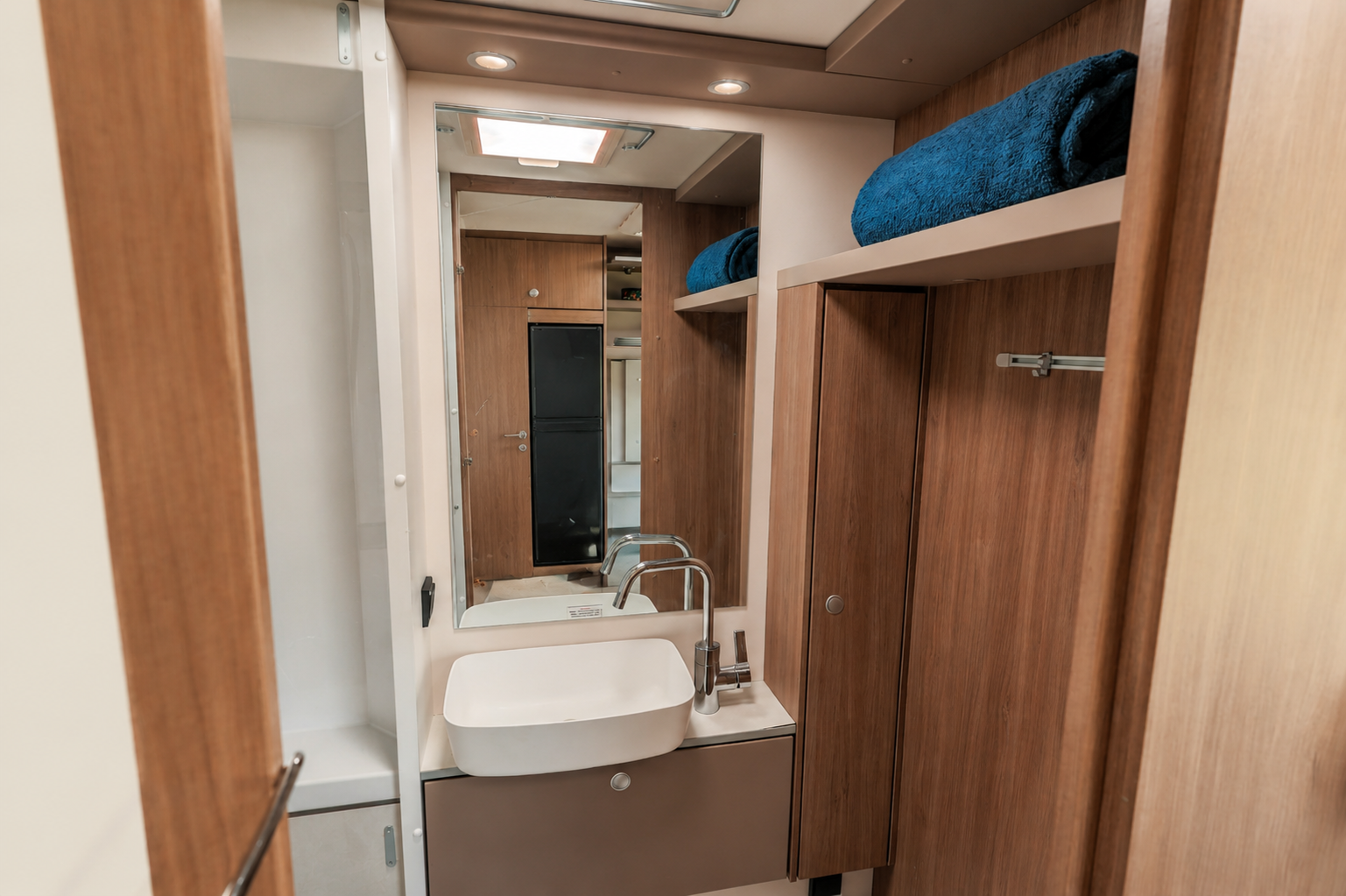 Van bathroom interior with sink, mirror, storage cabinets, towel shelf, wood paneling, and ceiling light visible.